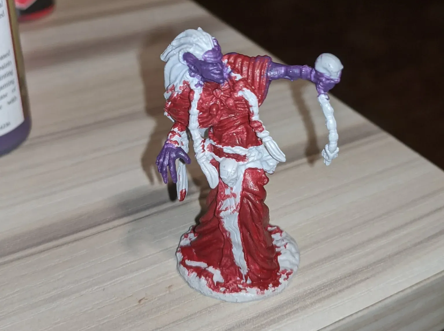 Miniature figure of a purple-skinned sorceress with white hair and red and white robes, holding a skull.