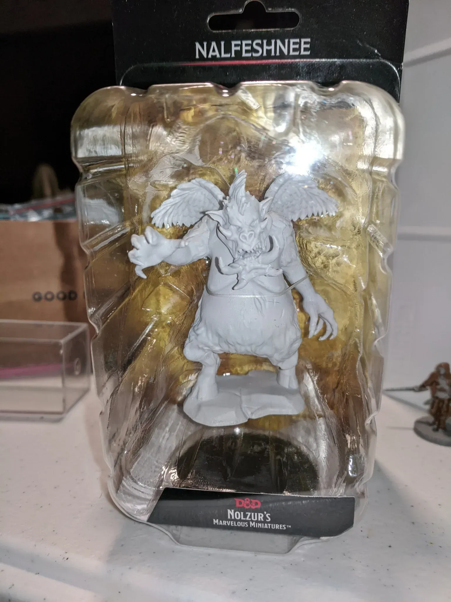 Figure of a Nalfeshnee demon in plastic packaging. Gray figure with wings and clawed hands on a base.