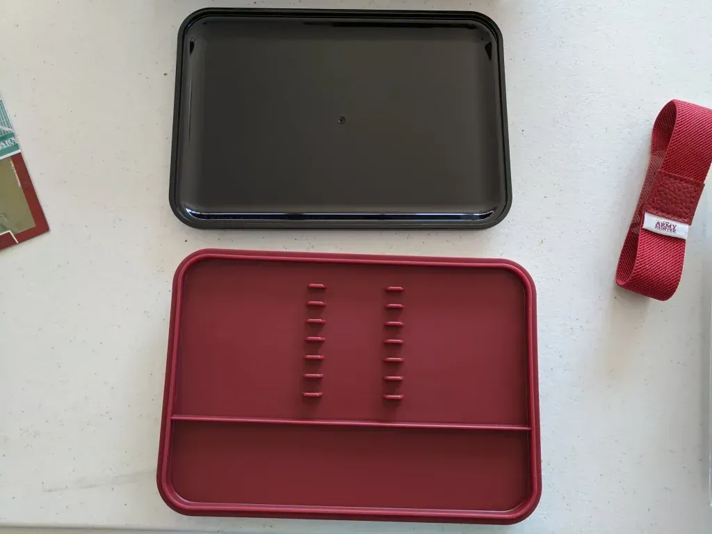 Open red and black craft box with tray and spool of red ribbon on white surface.