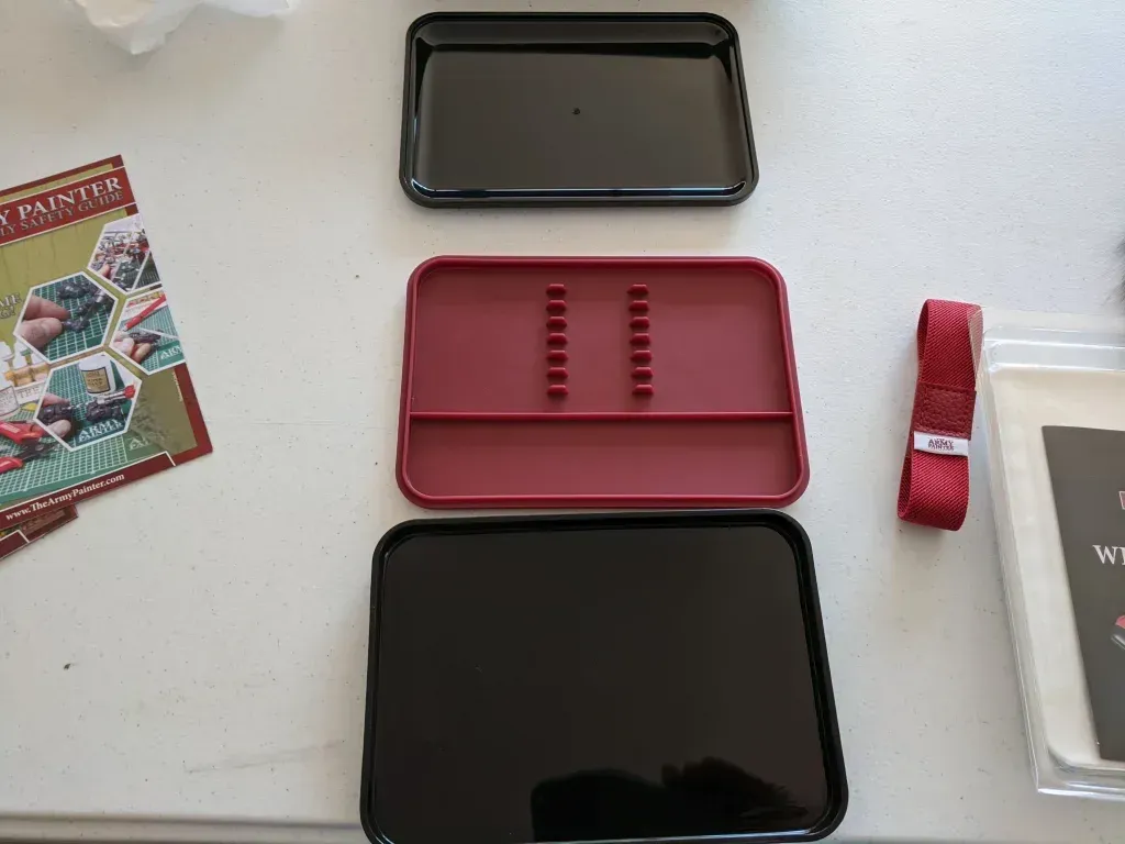 Three rectangular trays: black, red, and black. Red tray has slots. Ribbon and card visible.