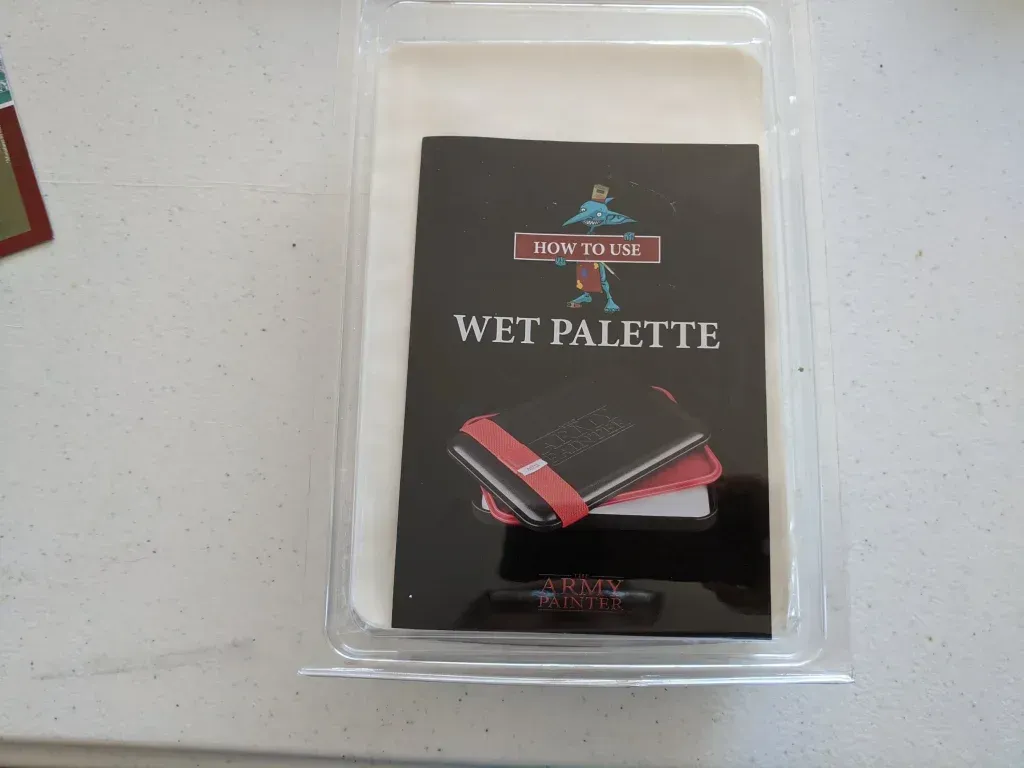 A black and red wet palette, in clear plastic packaging, on a white surface.