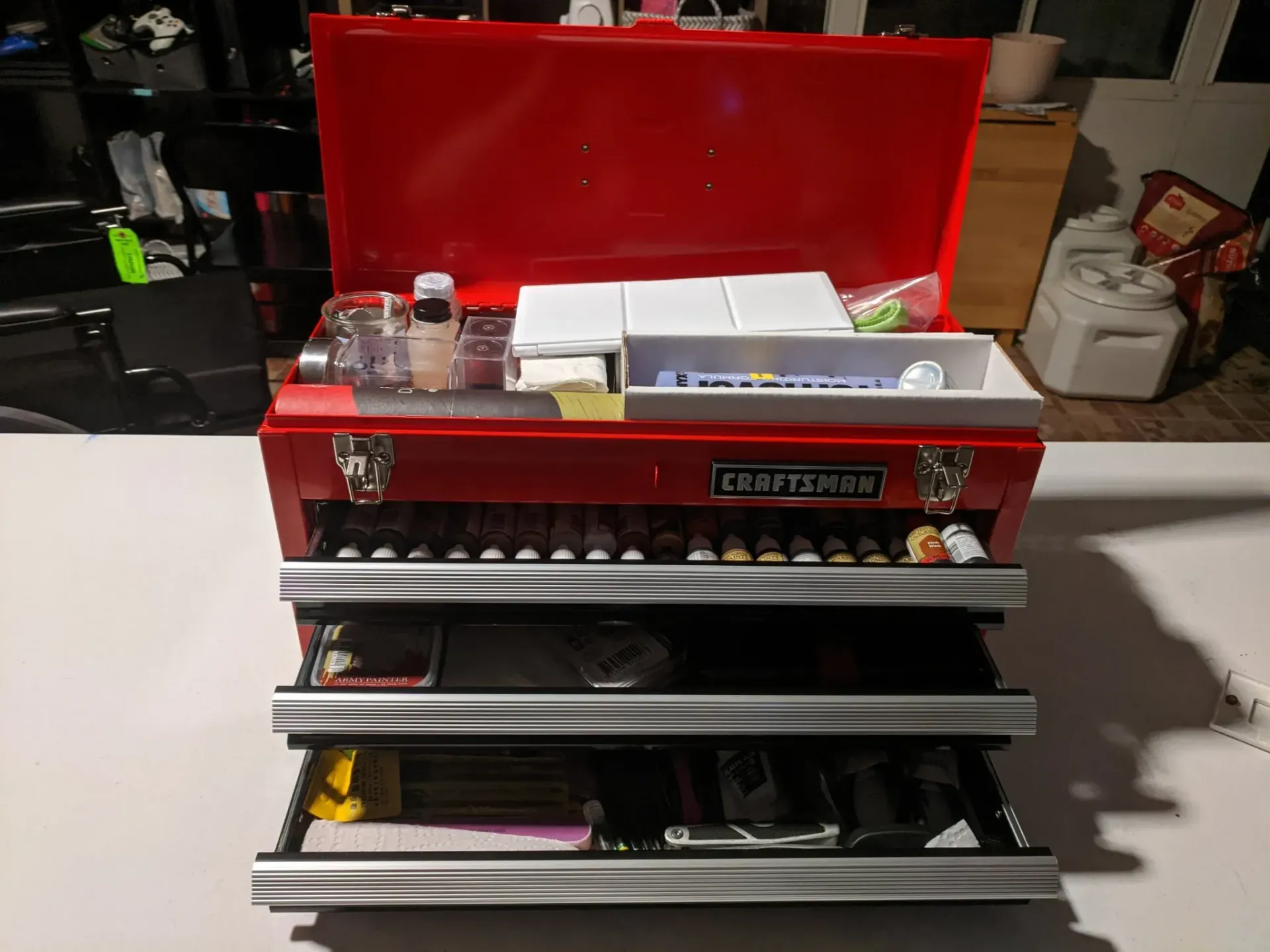 Red Craftsman toolbox with drawers open, filled with tools and supplies, on a table.