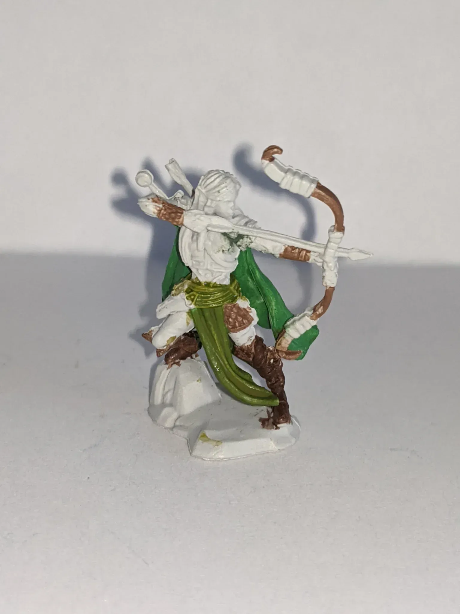 Miniature archer figure, poised to shoot. White and brown with green accents, on a white base.