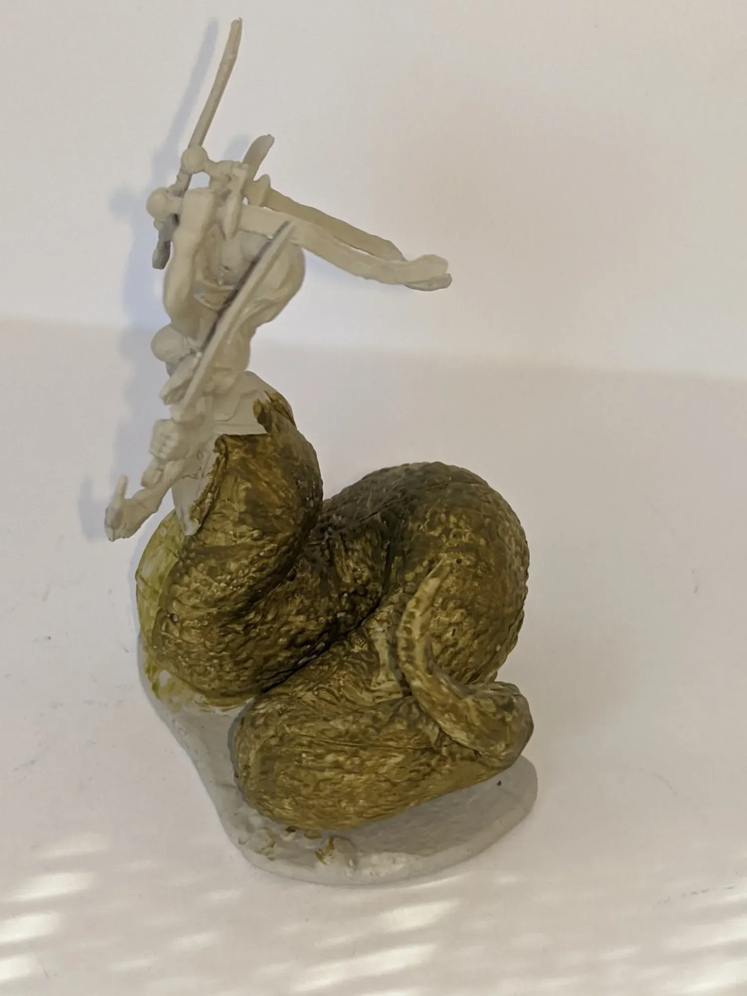 Sculpture of a warrior fighting a large, gold-colored serpent, atop a stone base.