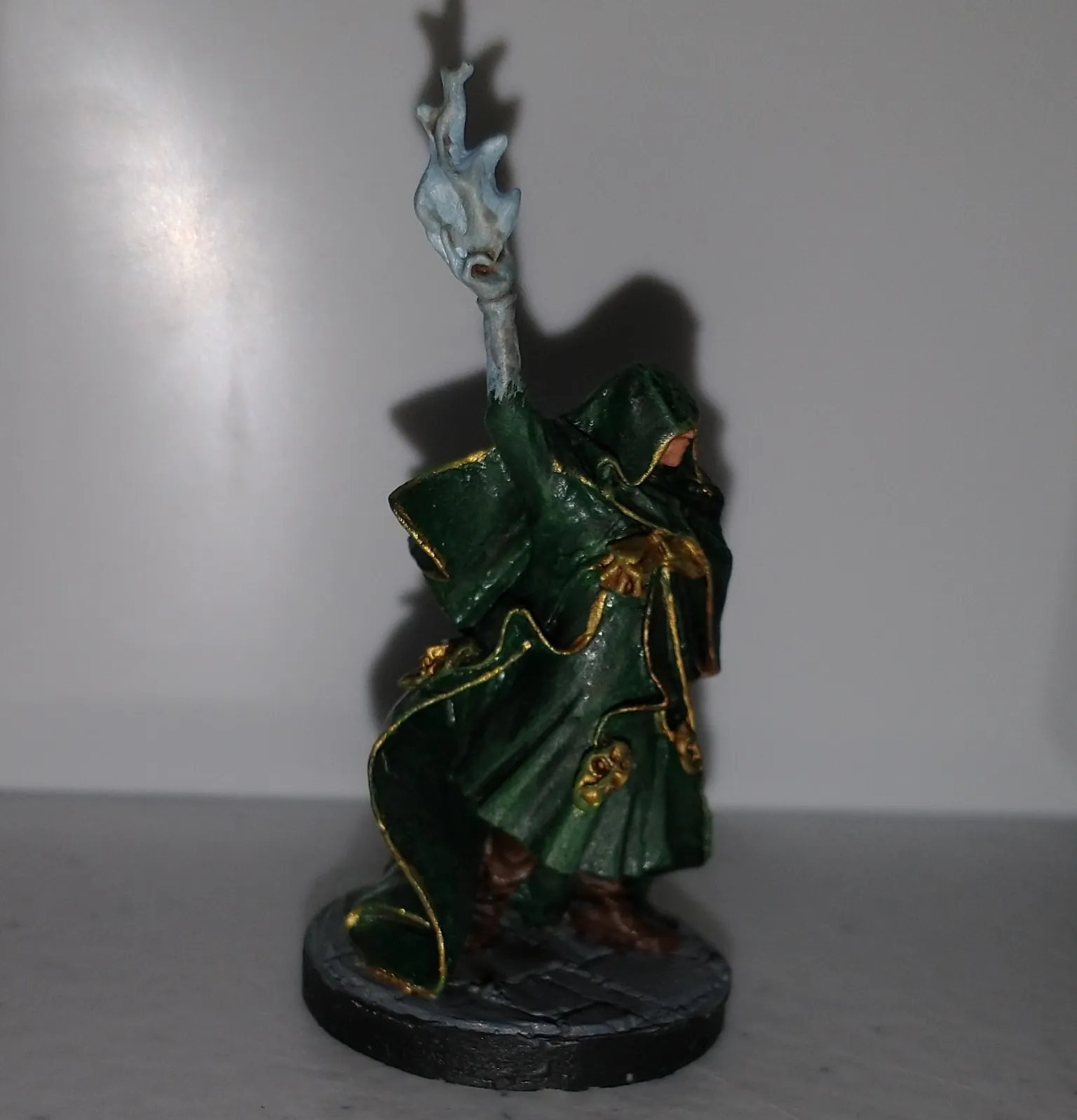 Miniature figure of a robed wizard in green, holding a staff with a blue flame.