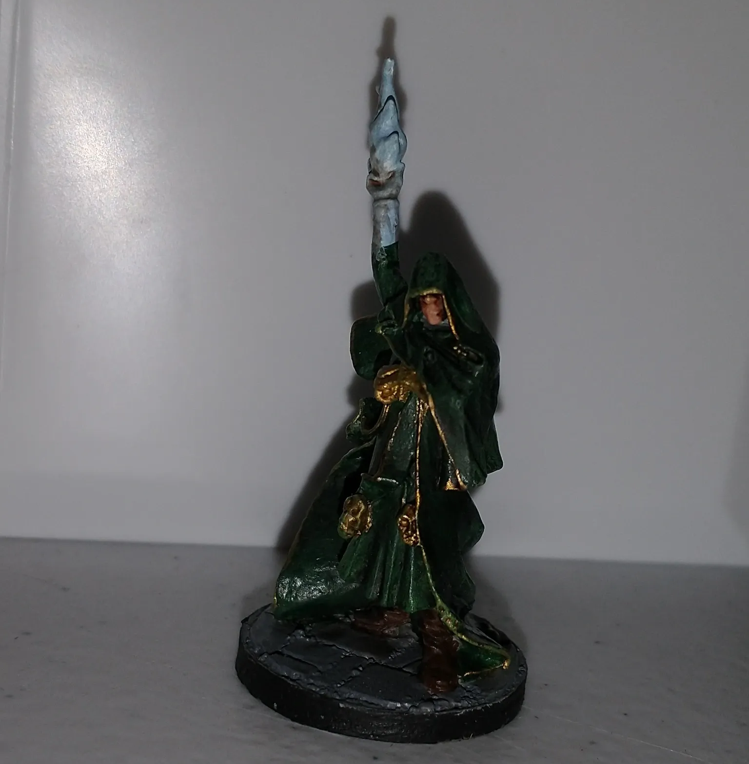 Miniature of an elf sorcerer in green robes, holding a staff with a blue crystal, on a gray base.