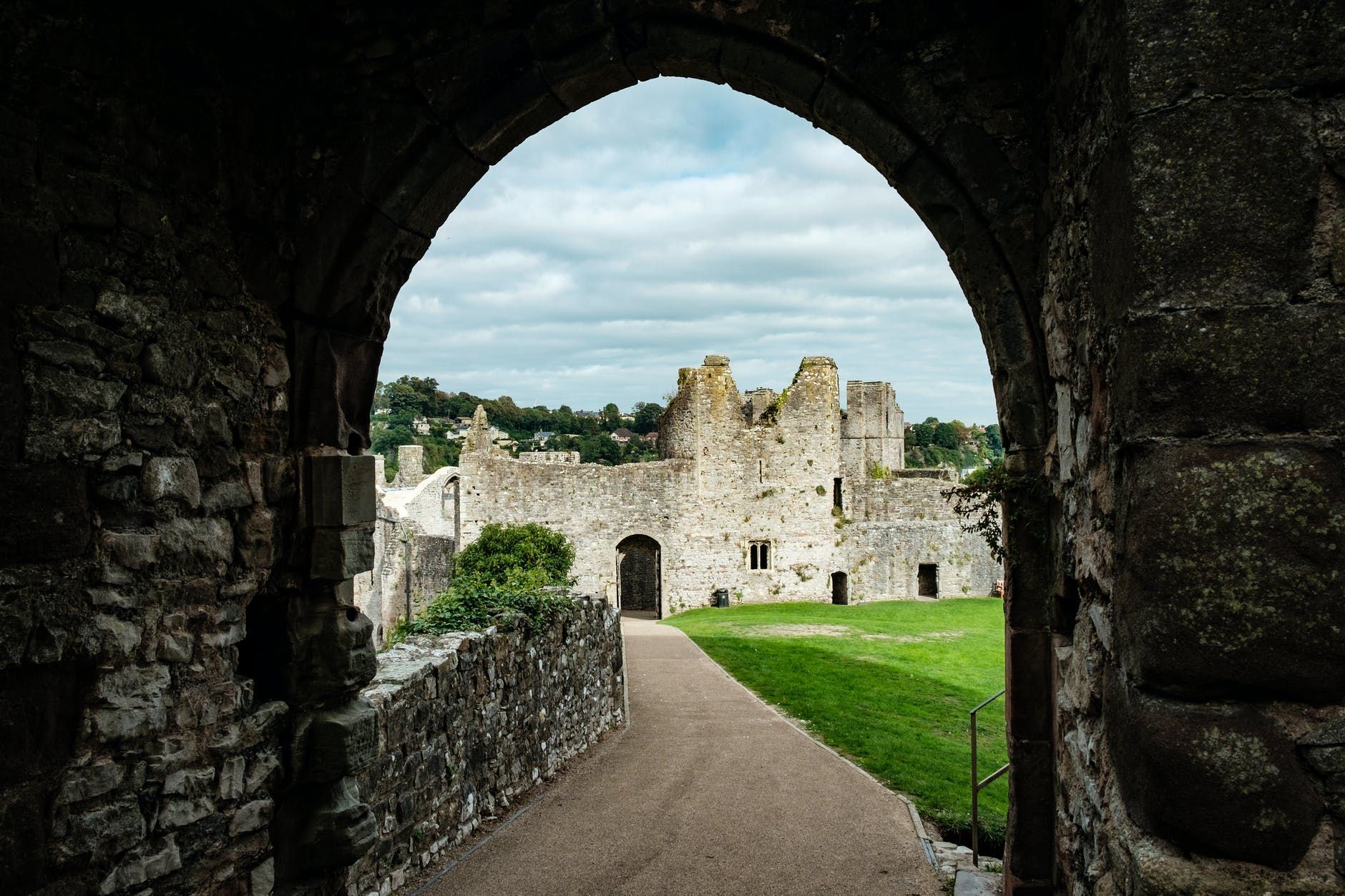 Stone archway framing a castle ruin on a grassy field under a cloudy sky.