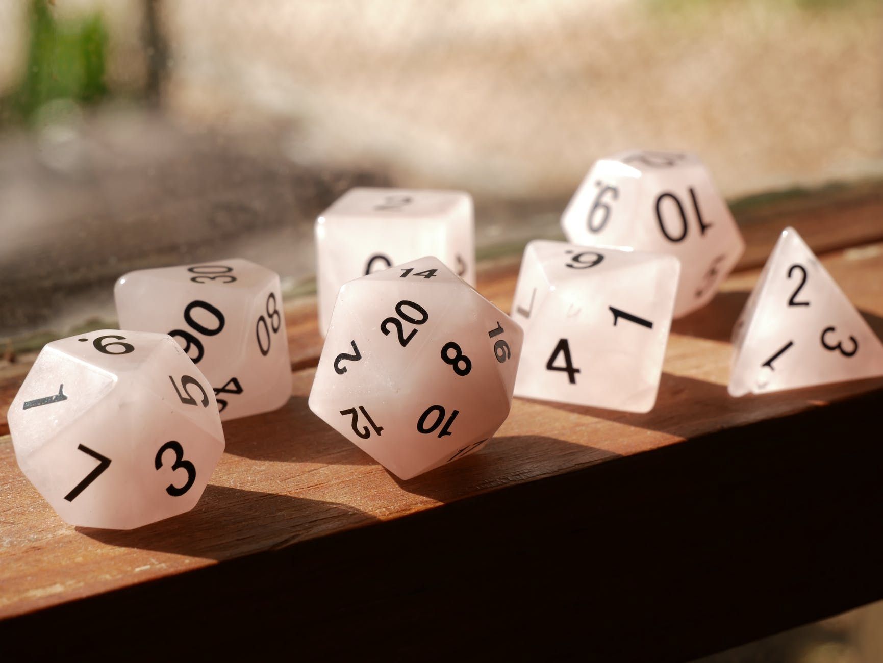 Seven translucent dice of various shapes and sizes on a wooden surface, lit by sunlight.