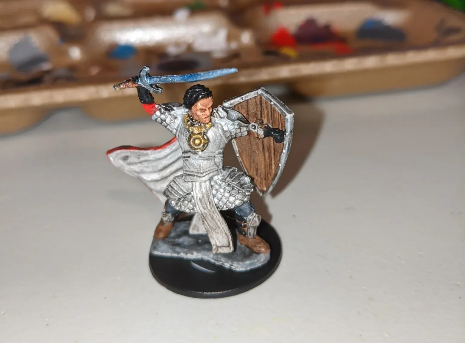Miniature figurine of a warrior in white armor, wielding a sword and shield, on a black base.