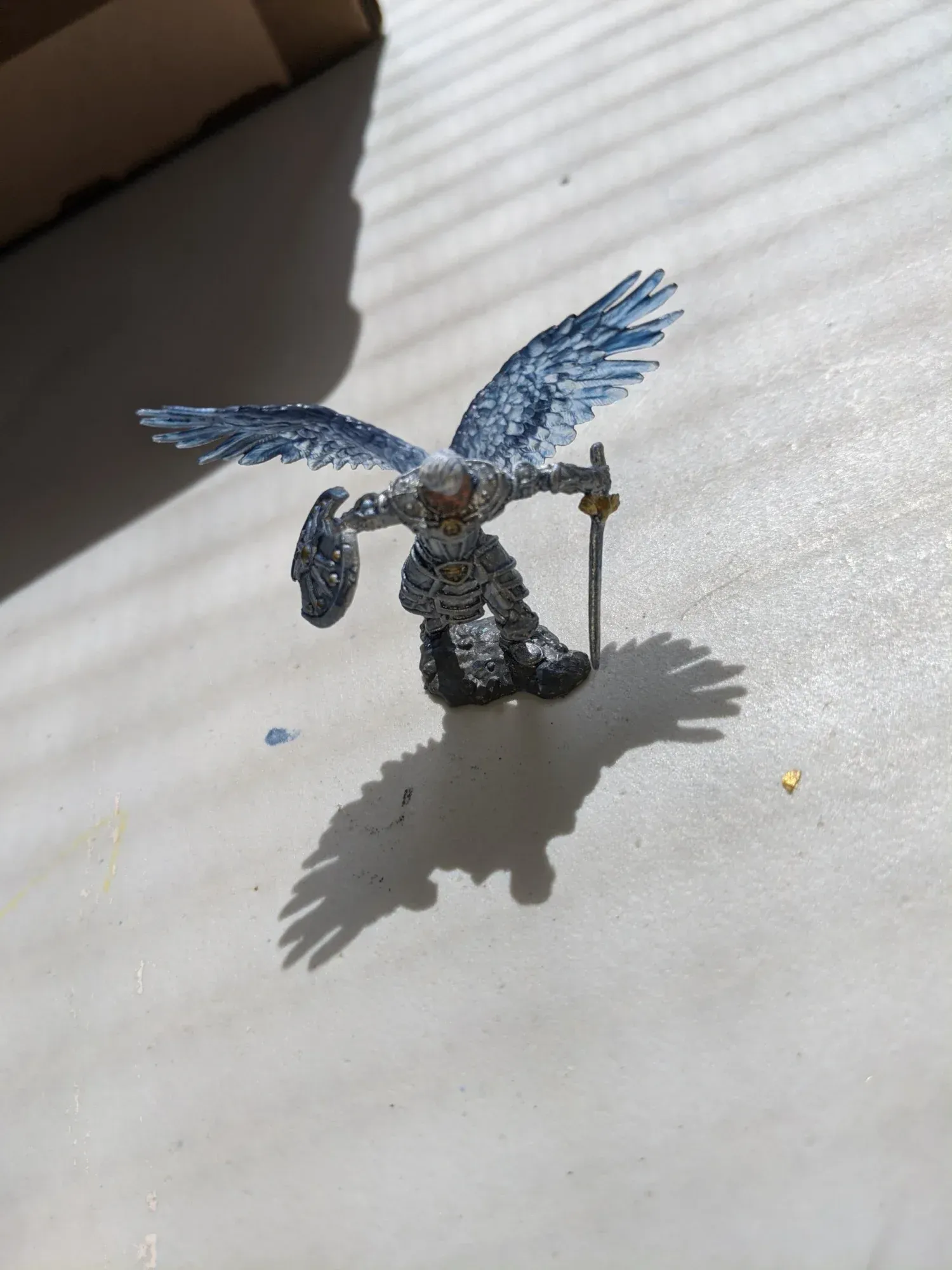 Miniature figurine of winged humanoid with sword and shield, painted in shades of blue and gray.