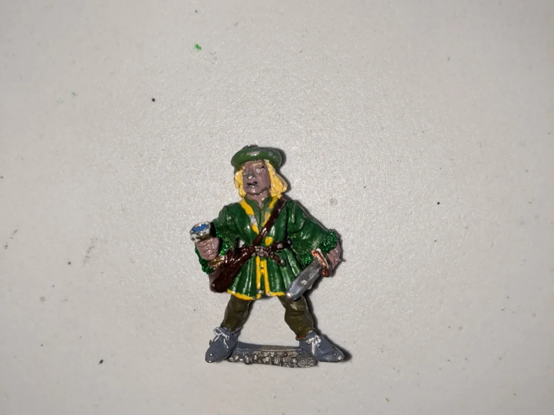 Miniature figure of a man in a green coat, hat, and boots. He is holding a weapon.