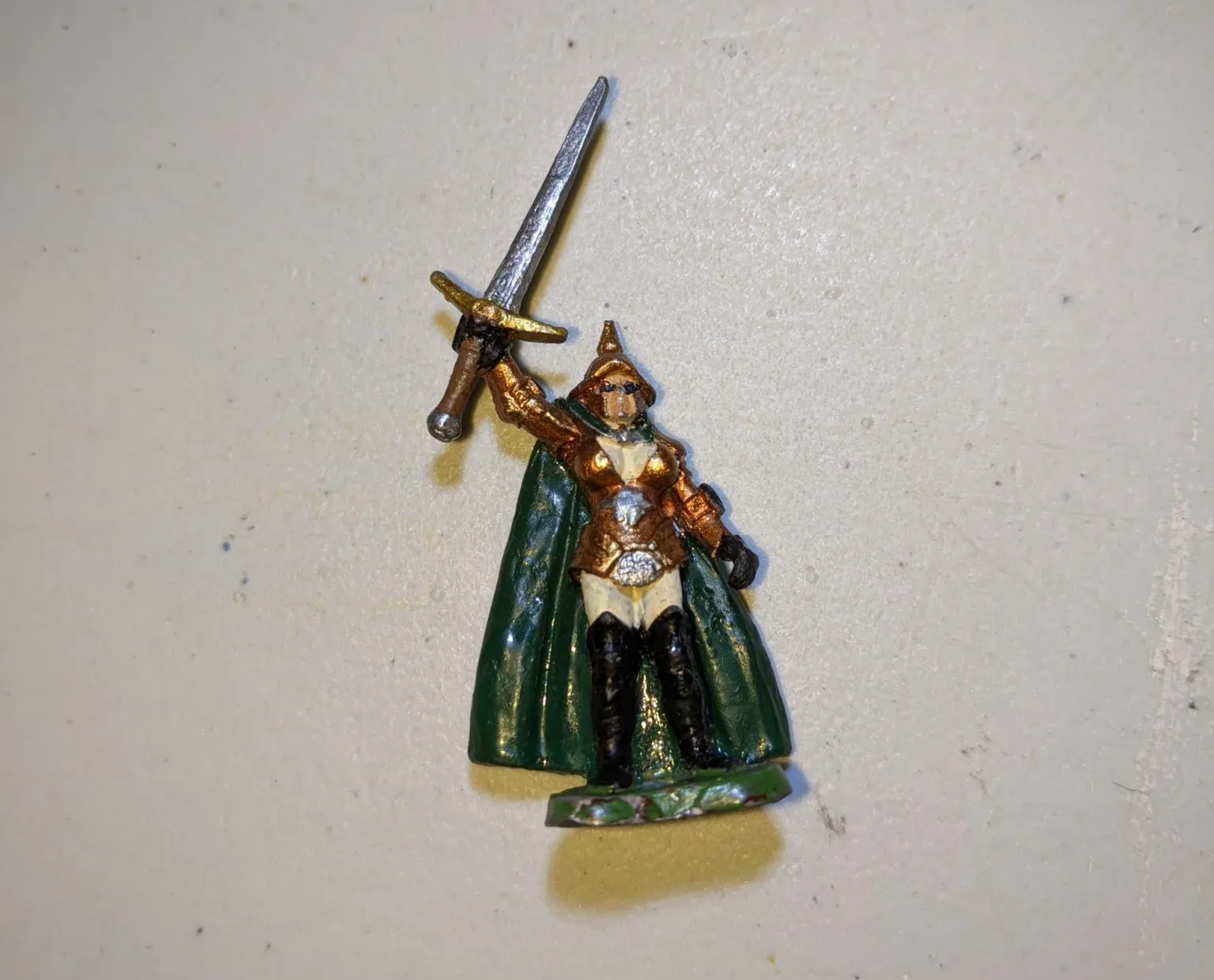 Miniature figure of a woman in gold armor, green cloak, holding a sword.