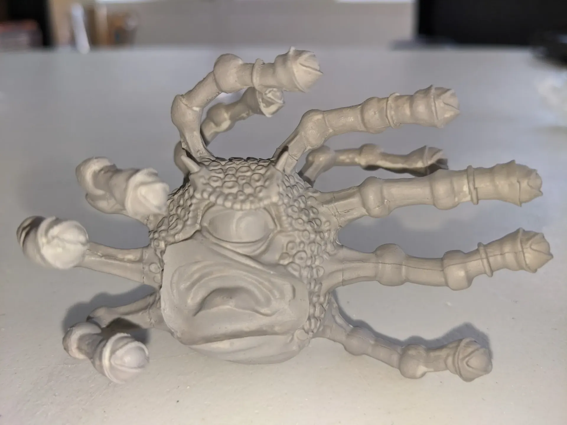 A gray, detailed model of a monster with multiple arms and eyes, set on a white surface.