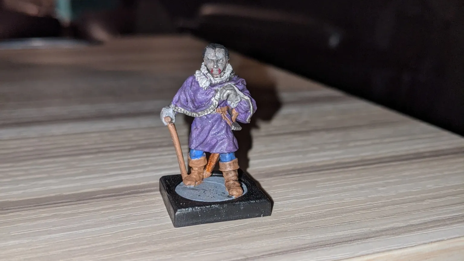 Miniature figure of a robed wizard in purple, holding a staff, on a wooden table.