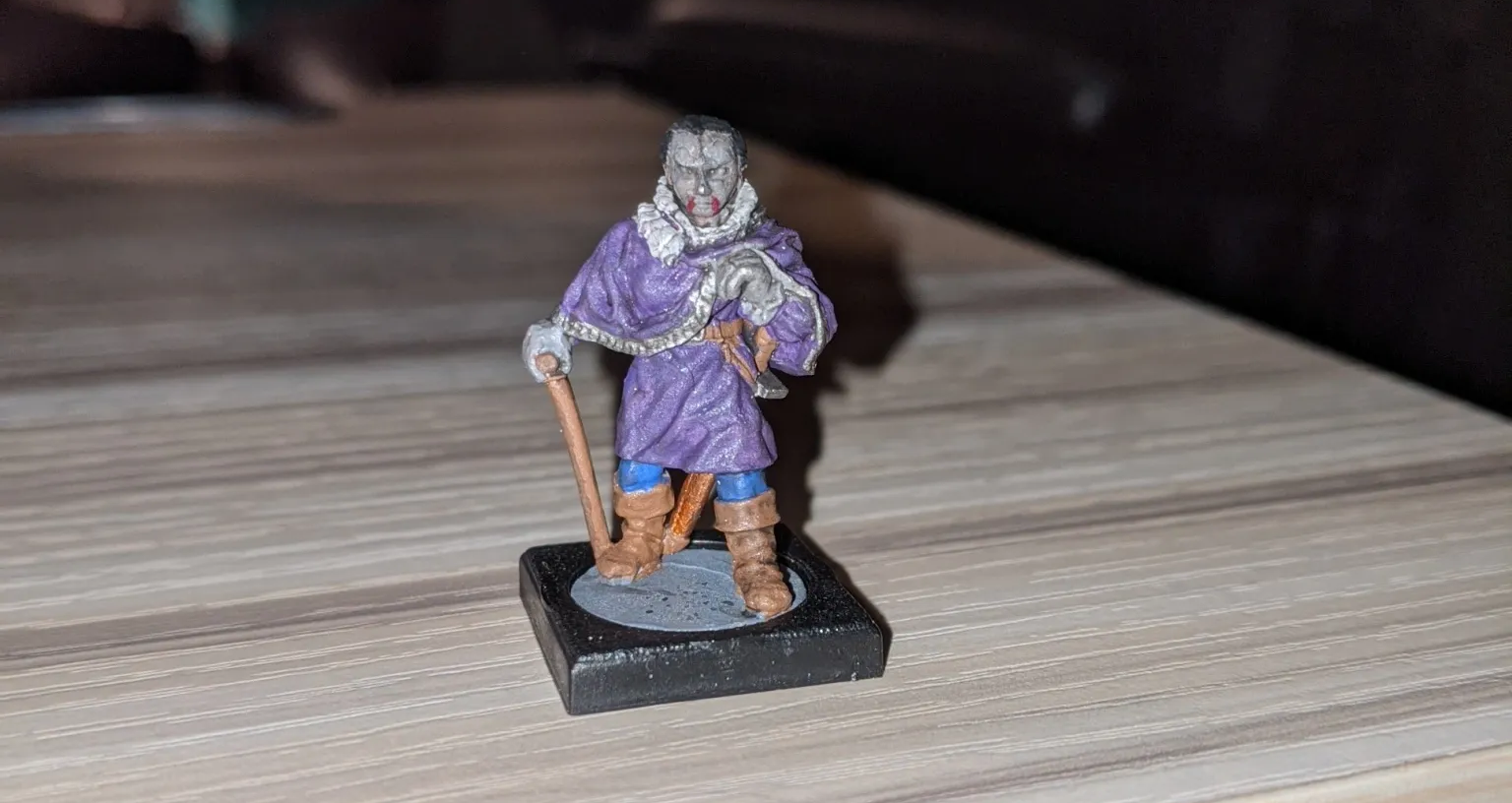 Miniature figure of a robed person in purple with white fur and a staff, on a black square base.