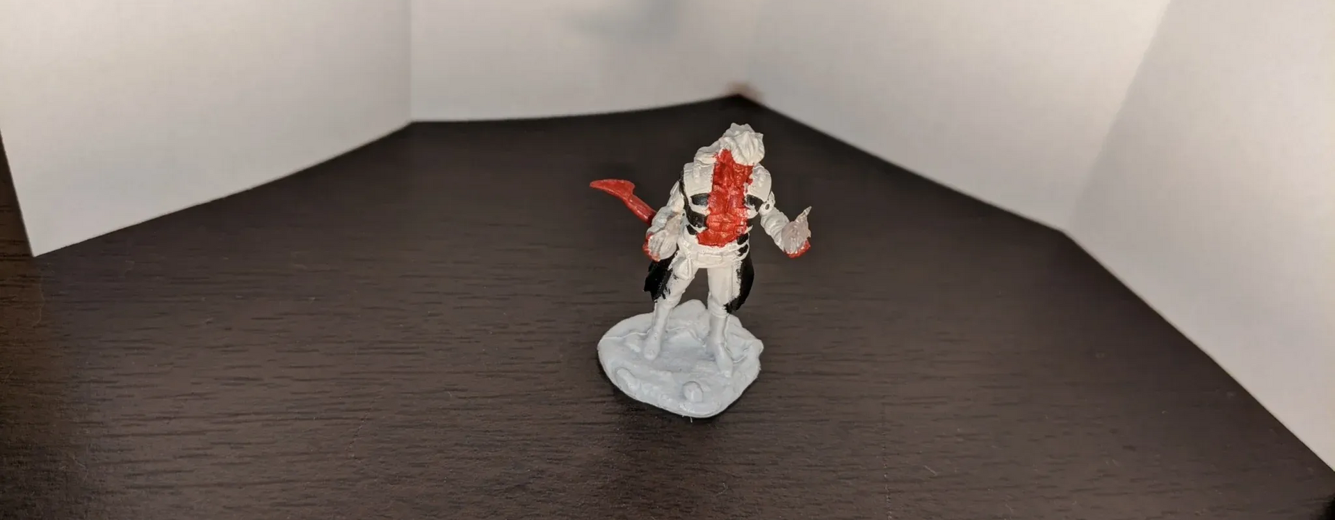 A white and red figure on a base in front of a corner made of white paper.