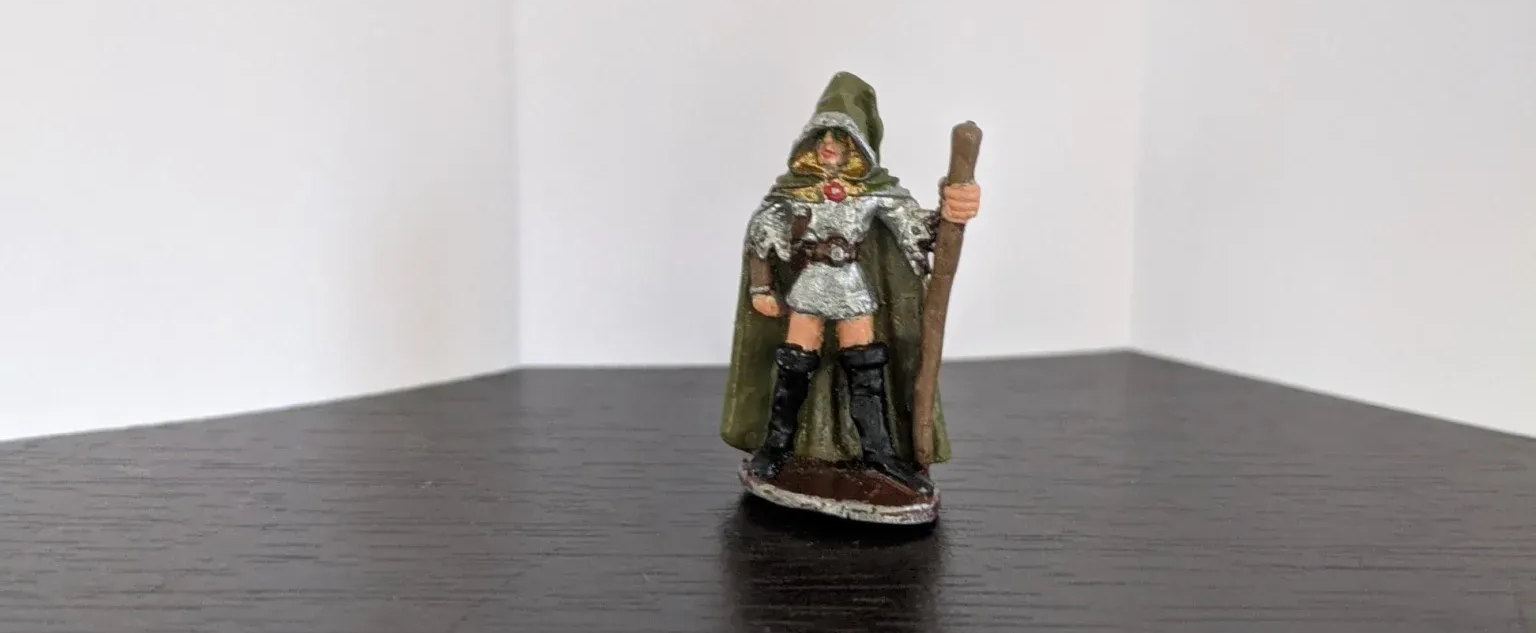 A figurine of a cloaked figure with a staff, standing on a dark surface in a white room.