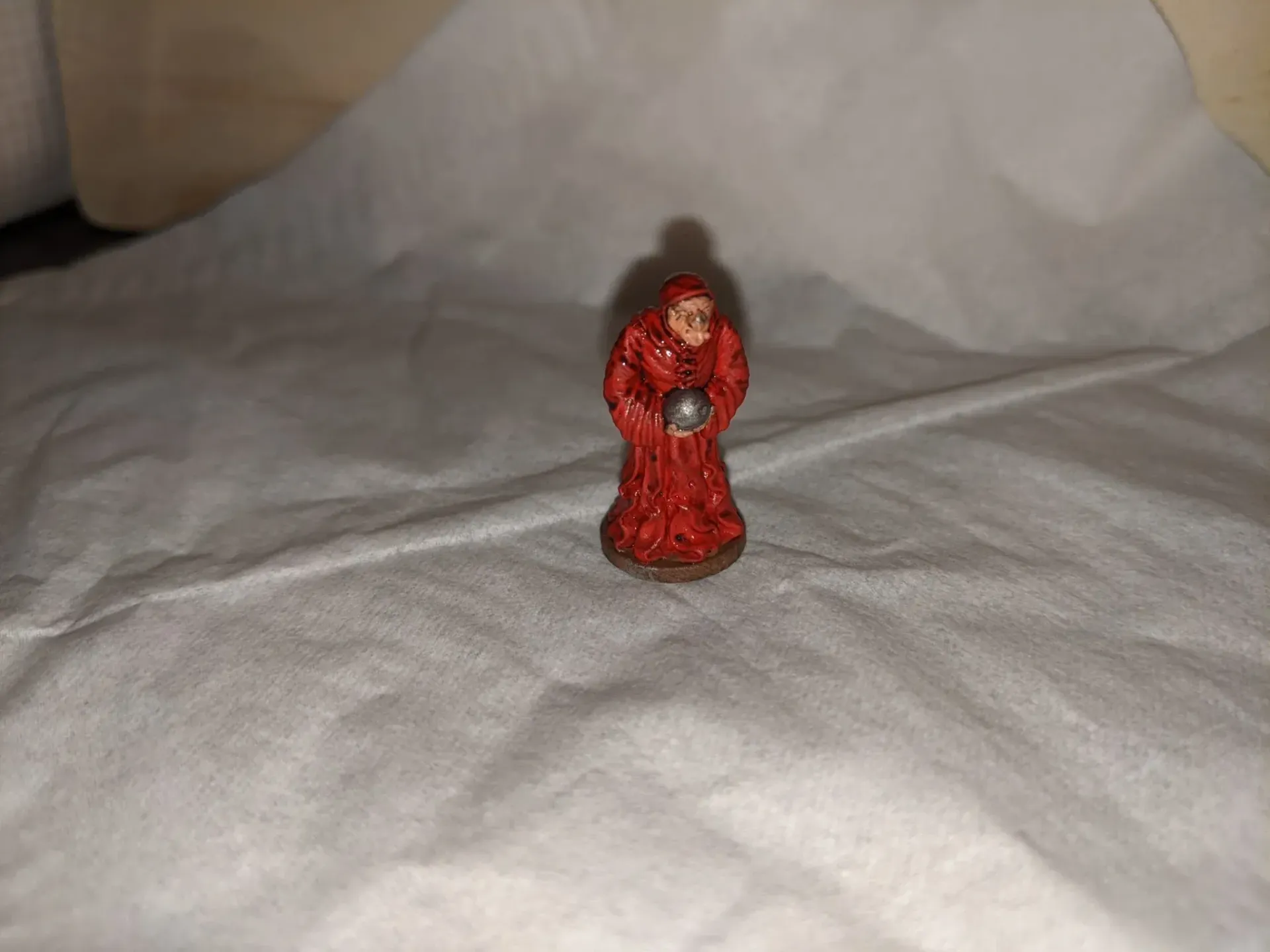 Miniature figurine of a robed figure in red, holding a silver orb, on a white background.