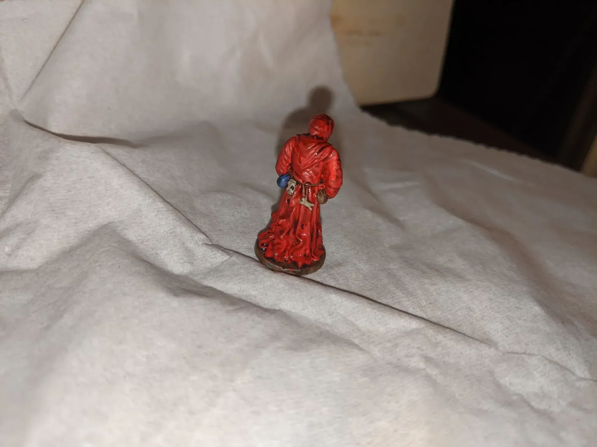 Red miniature figure on white surface, wearing a robe and standing.