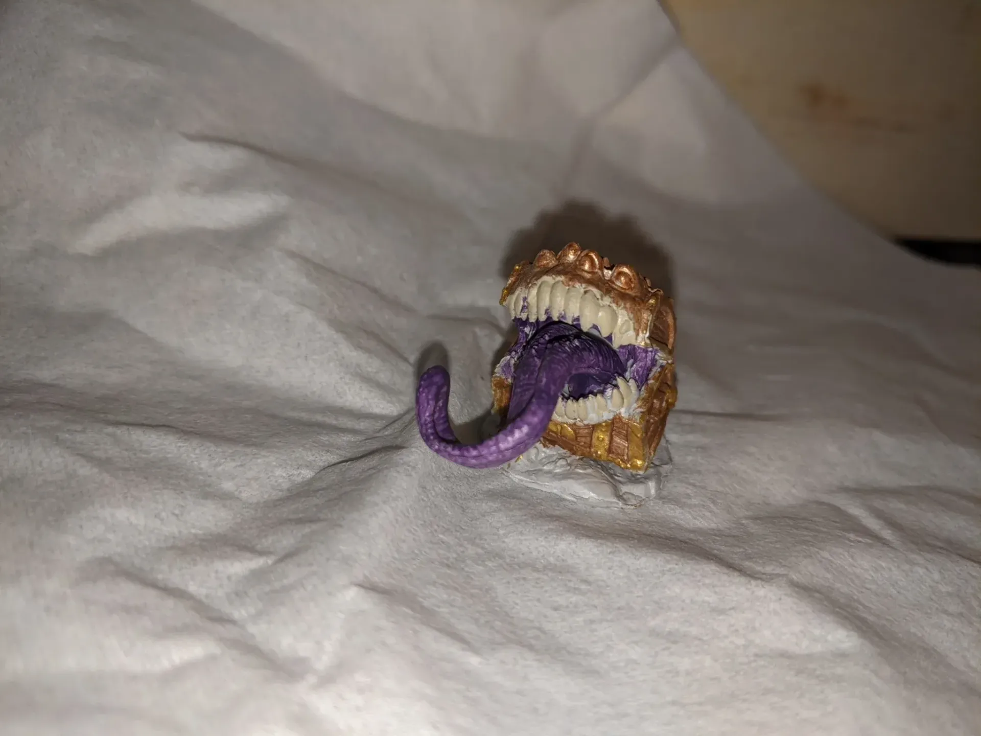 A small, open-mouthed creature with sharp teeth and a long purple tongue, set on a white surface.
