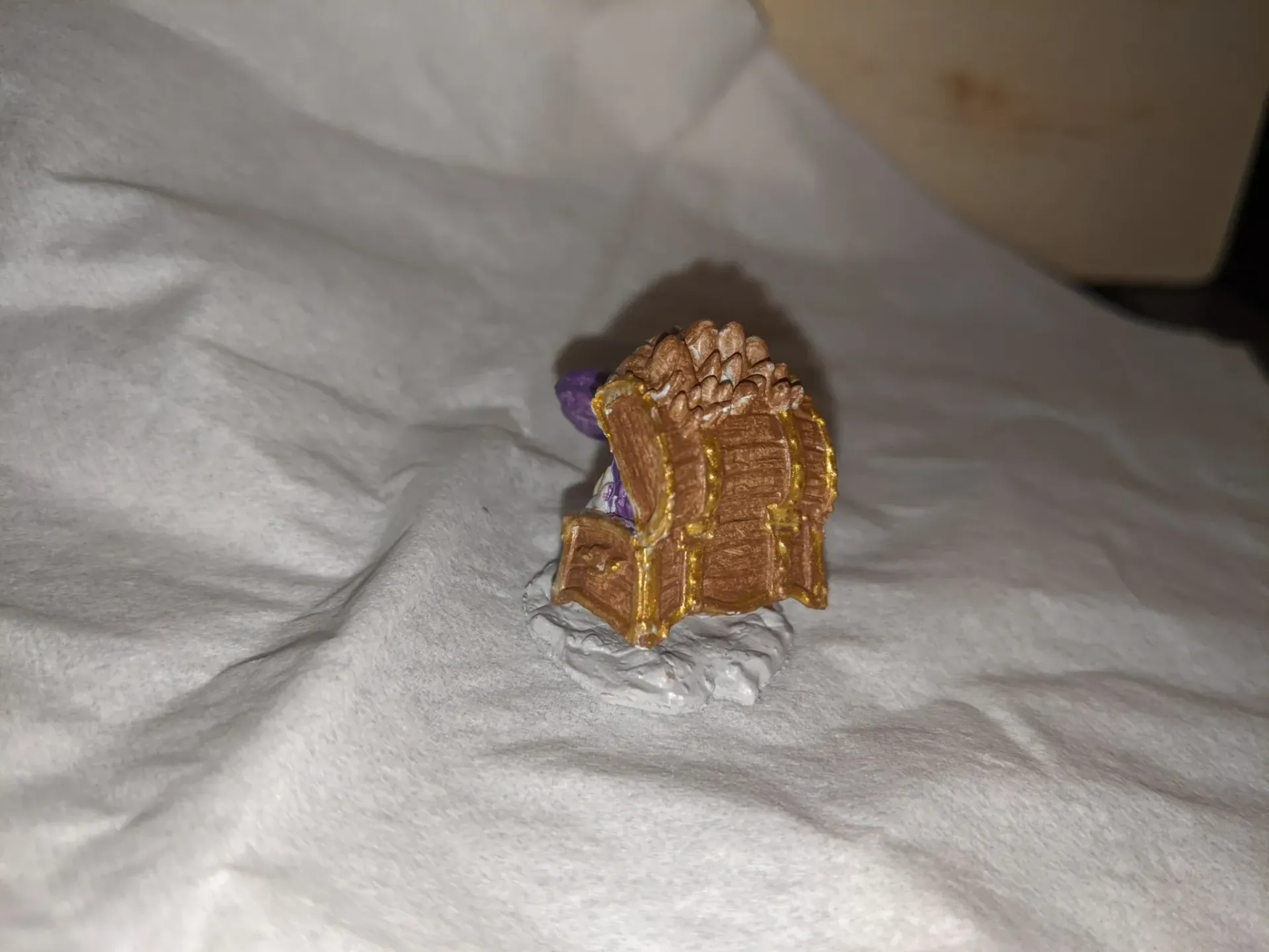 Miniature brown and gold chest overflowing with brown treasure on a textured white surface.