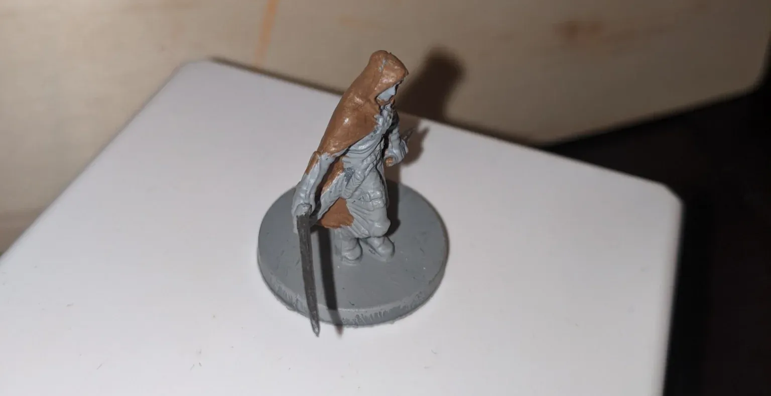 Miniature figure with brown hood and gray clothing on a gray circular base.