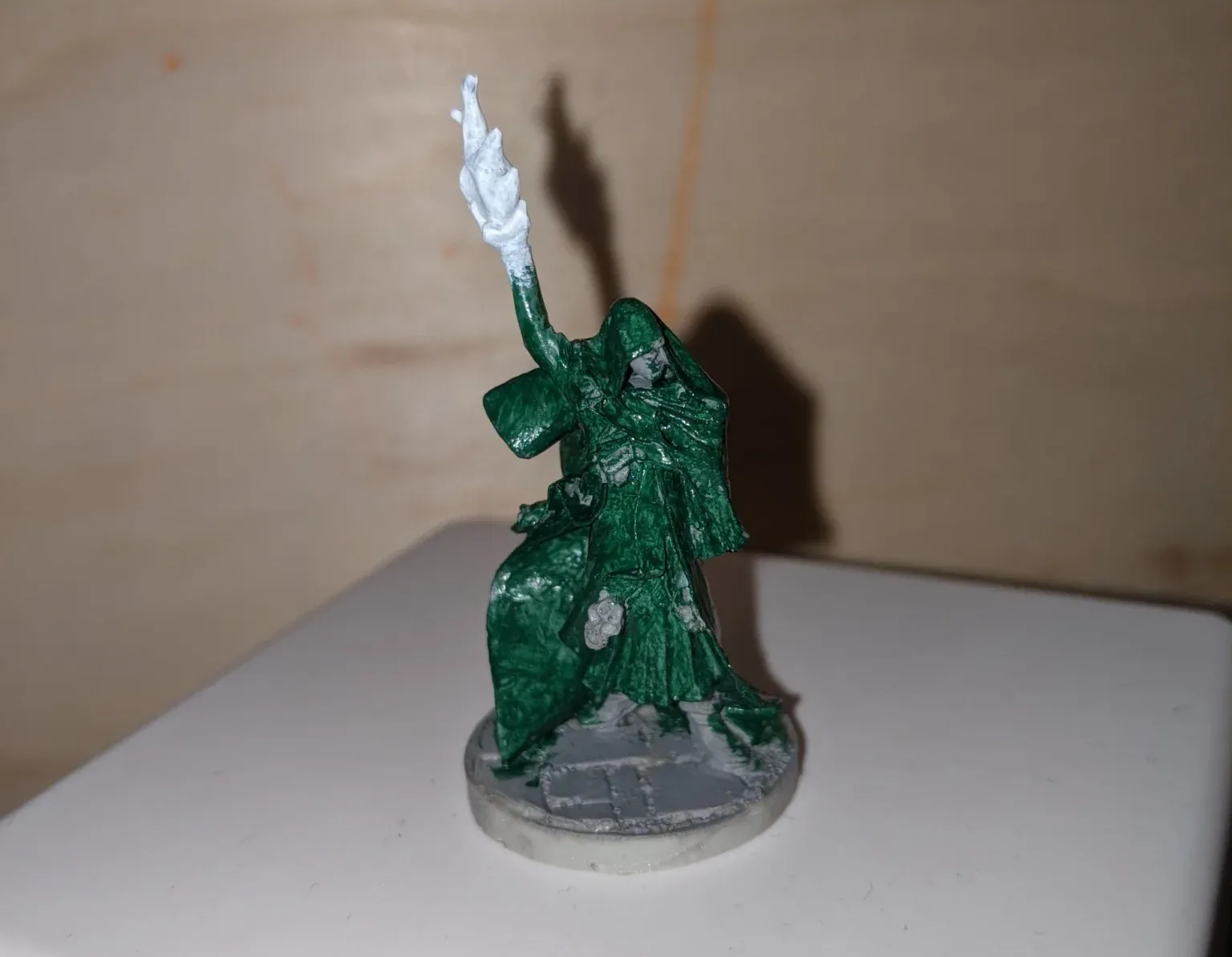 Green cloaked miniature figure with raised arm holding a white flame, on a gray and white base.