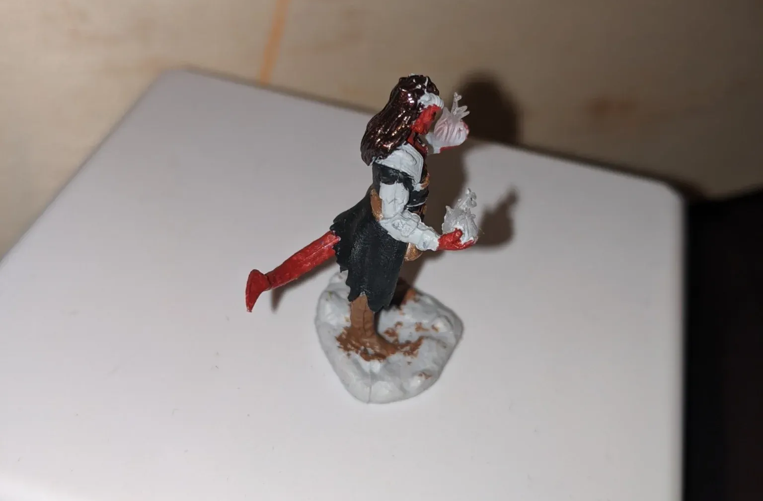 Miniature figurine of a demon-like figure with red skin, holding a flower, atop a snowy base.