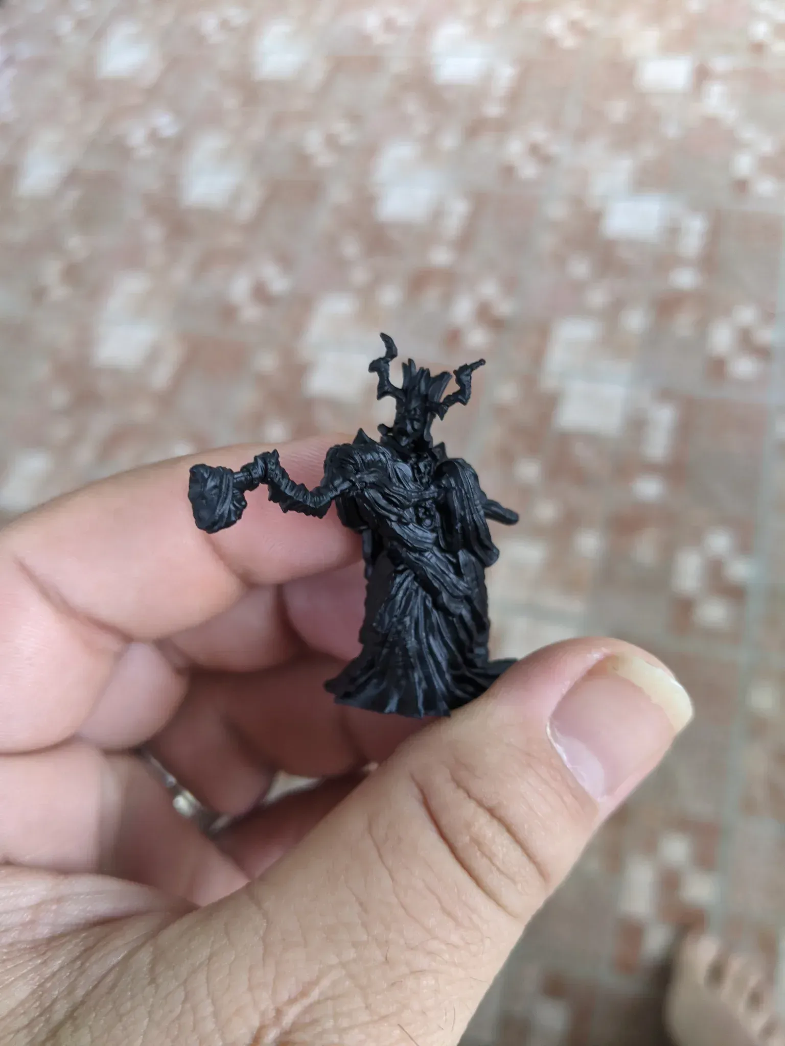 Miniature of a dark, tree-like creature holding a small object, held in a hand against a blurred background.