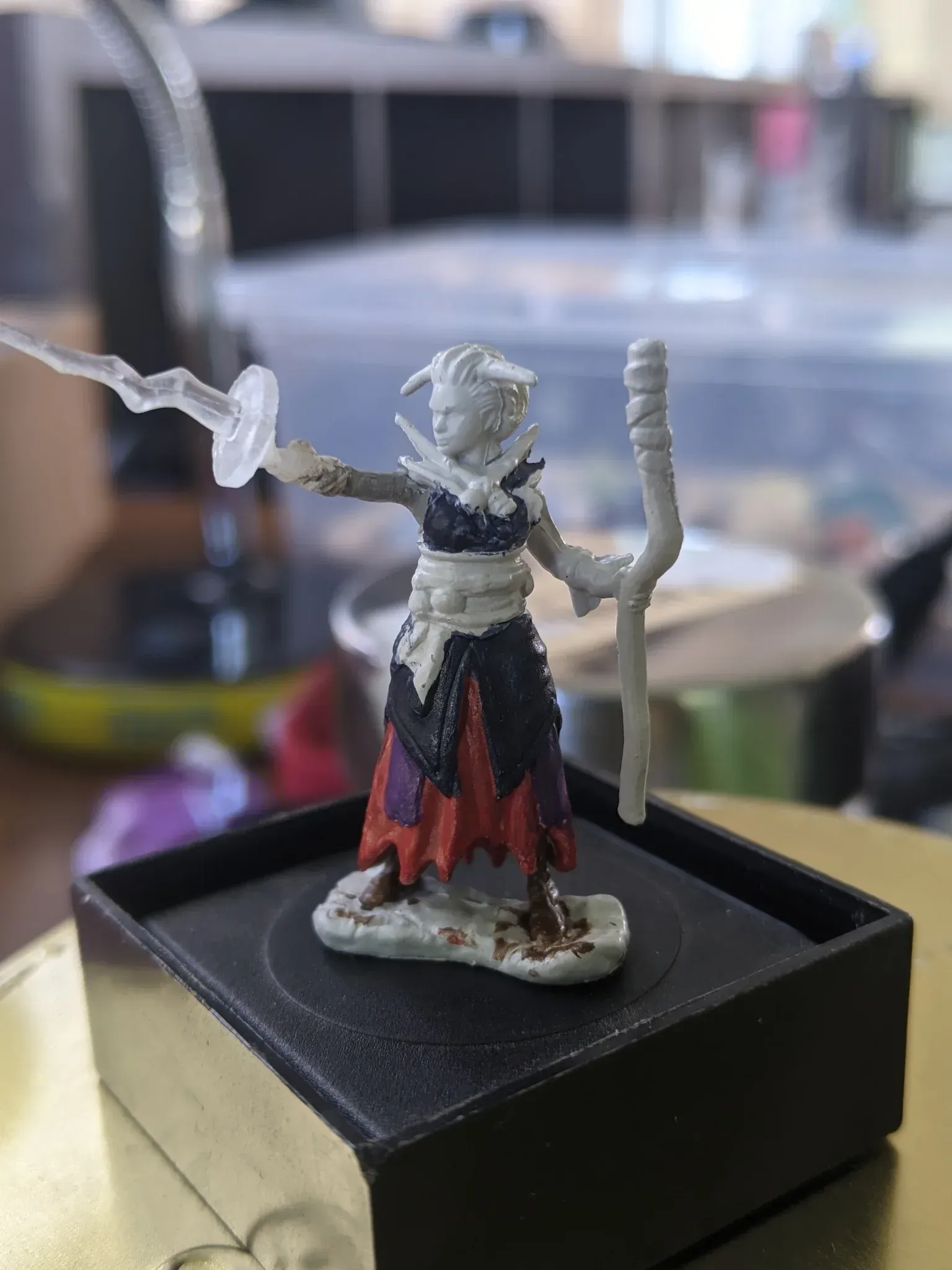 Miniature female wizard, casting a spell, with staff, on a black base. She wears a dark outfit with orange and red accents.
