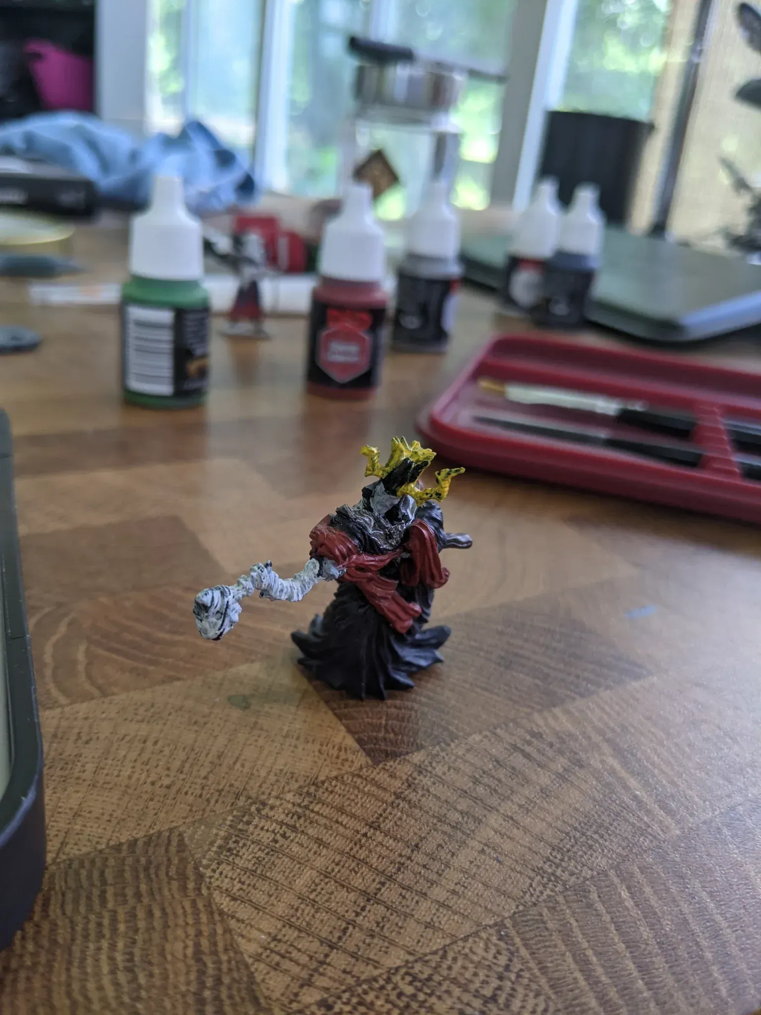 Miniature figure of a skeleton king, painted with black, red, and gold, on a wooden table.