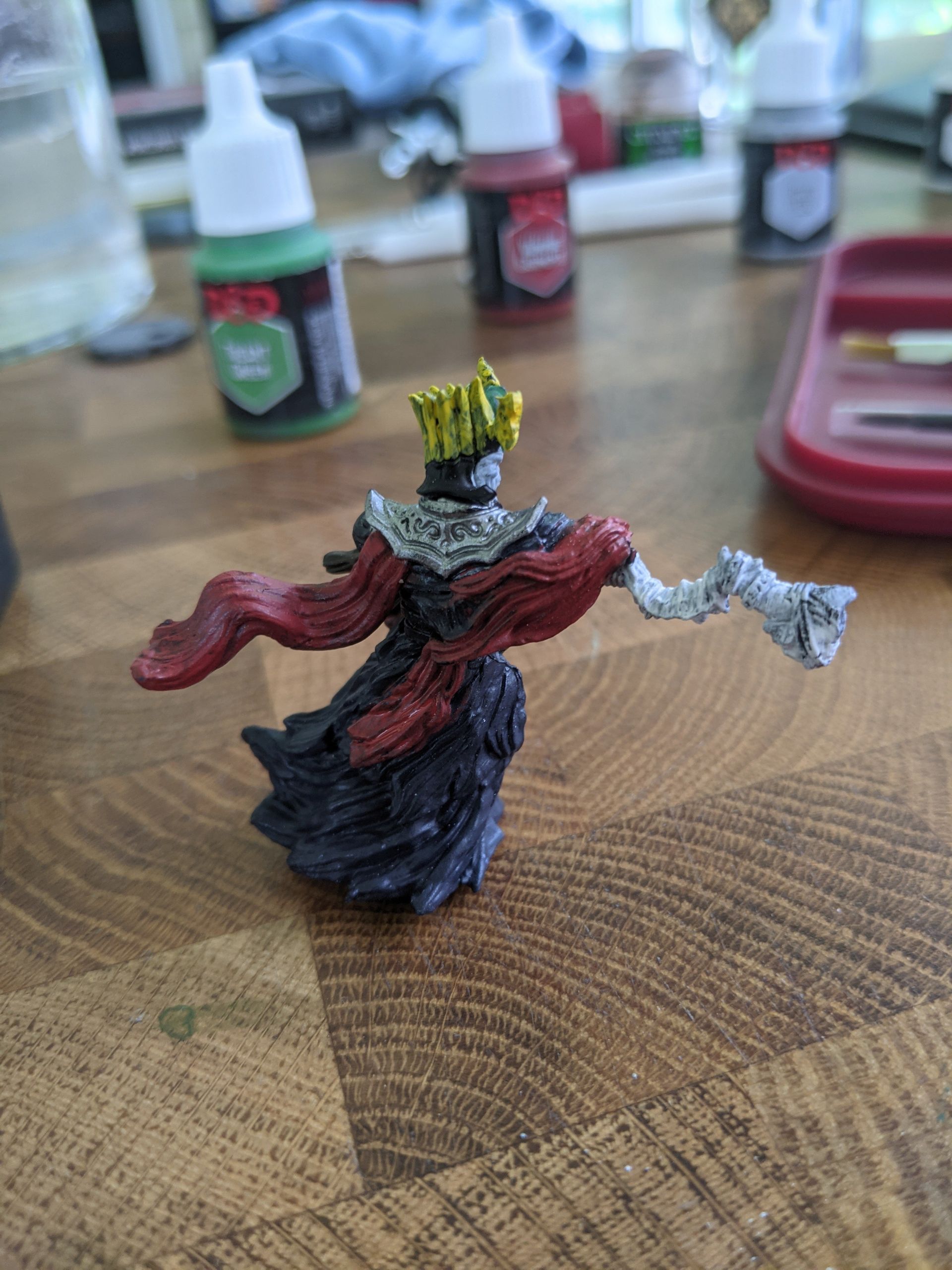 Miniature figure of a robed figure in a crown, with one arm outstretched. It is being painted on a table.