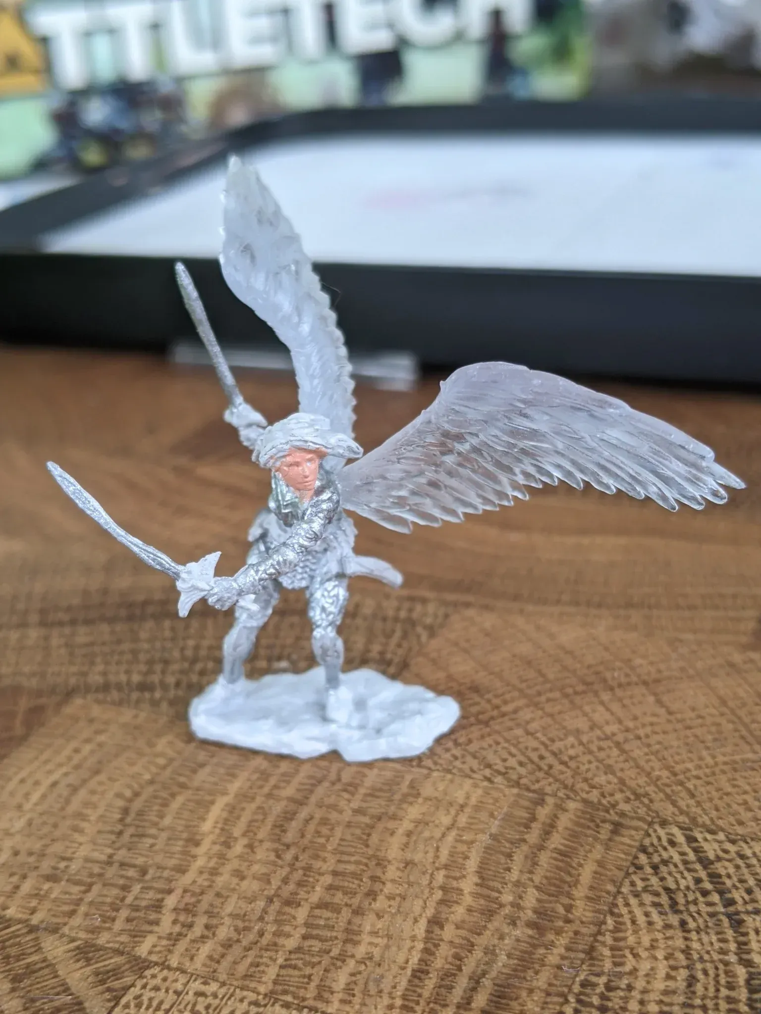 Miniature figure of a warrior with wings and swords, standing on a base.