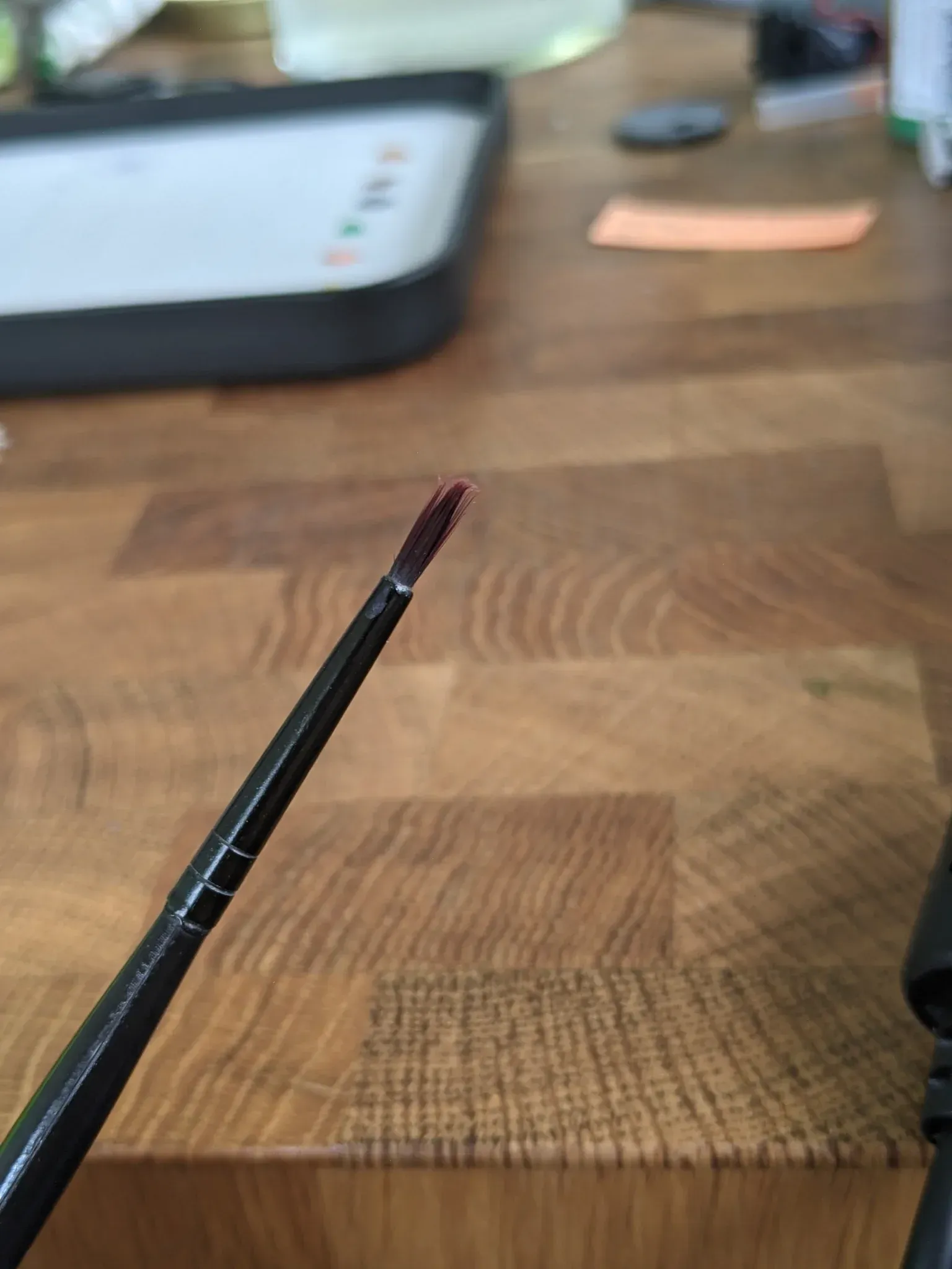A dark-handled paintbrush with dark-red paint on the bristles, on a wooden table.