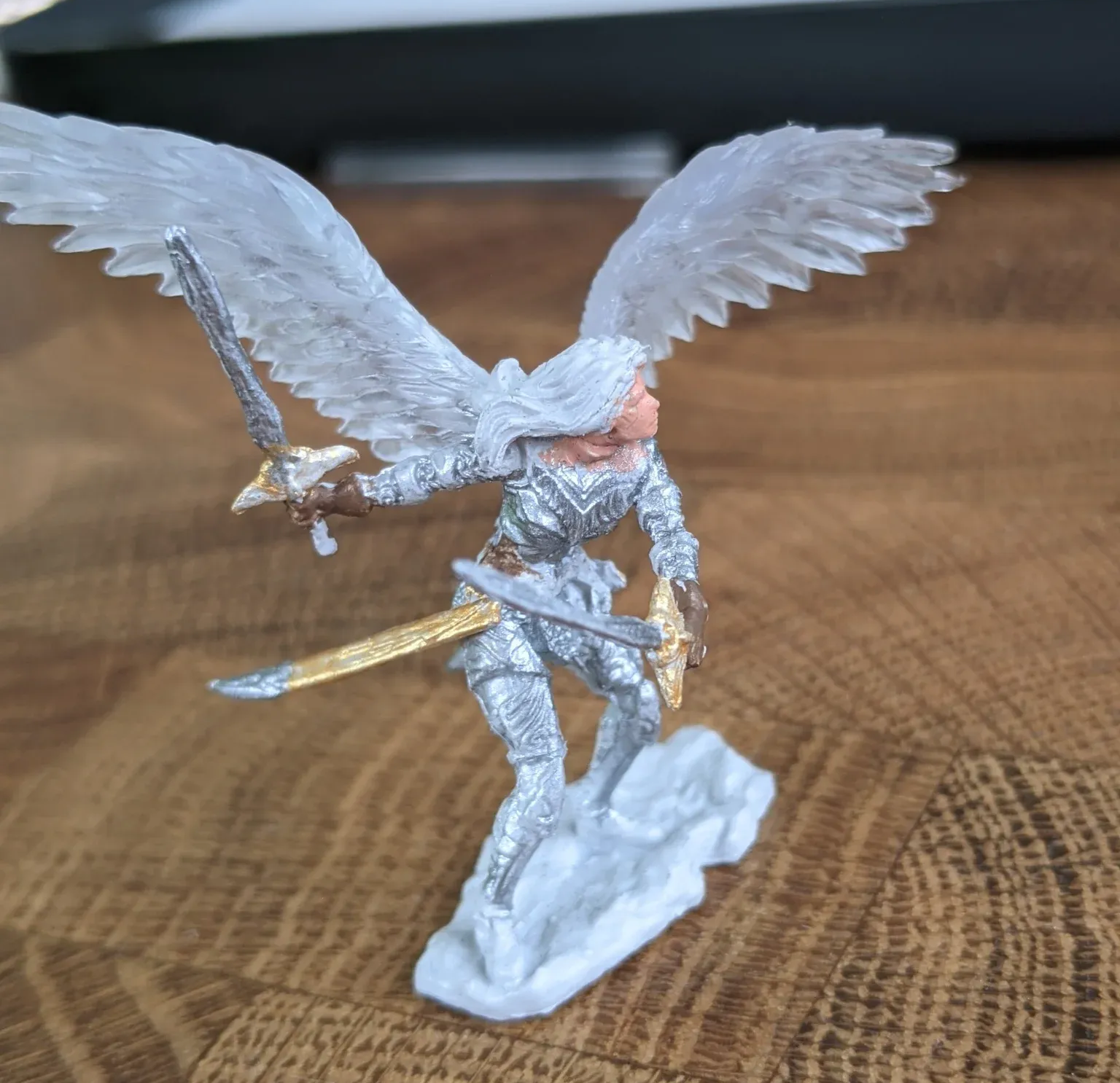 Miniature angel figure with silver armor, wings, and swords on a cloud base.