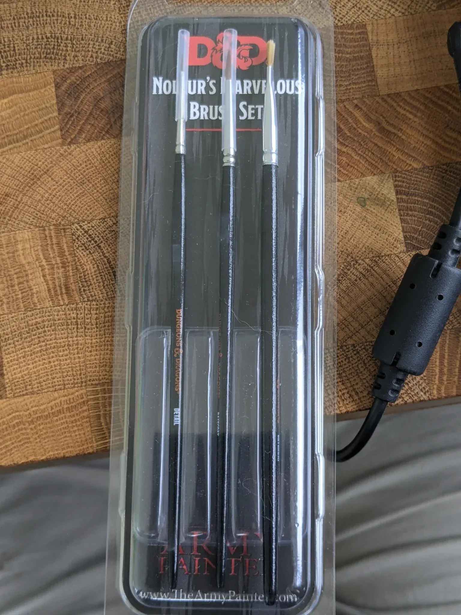 A sealed package of three black artist paint brushes on a wooden surface.