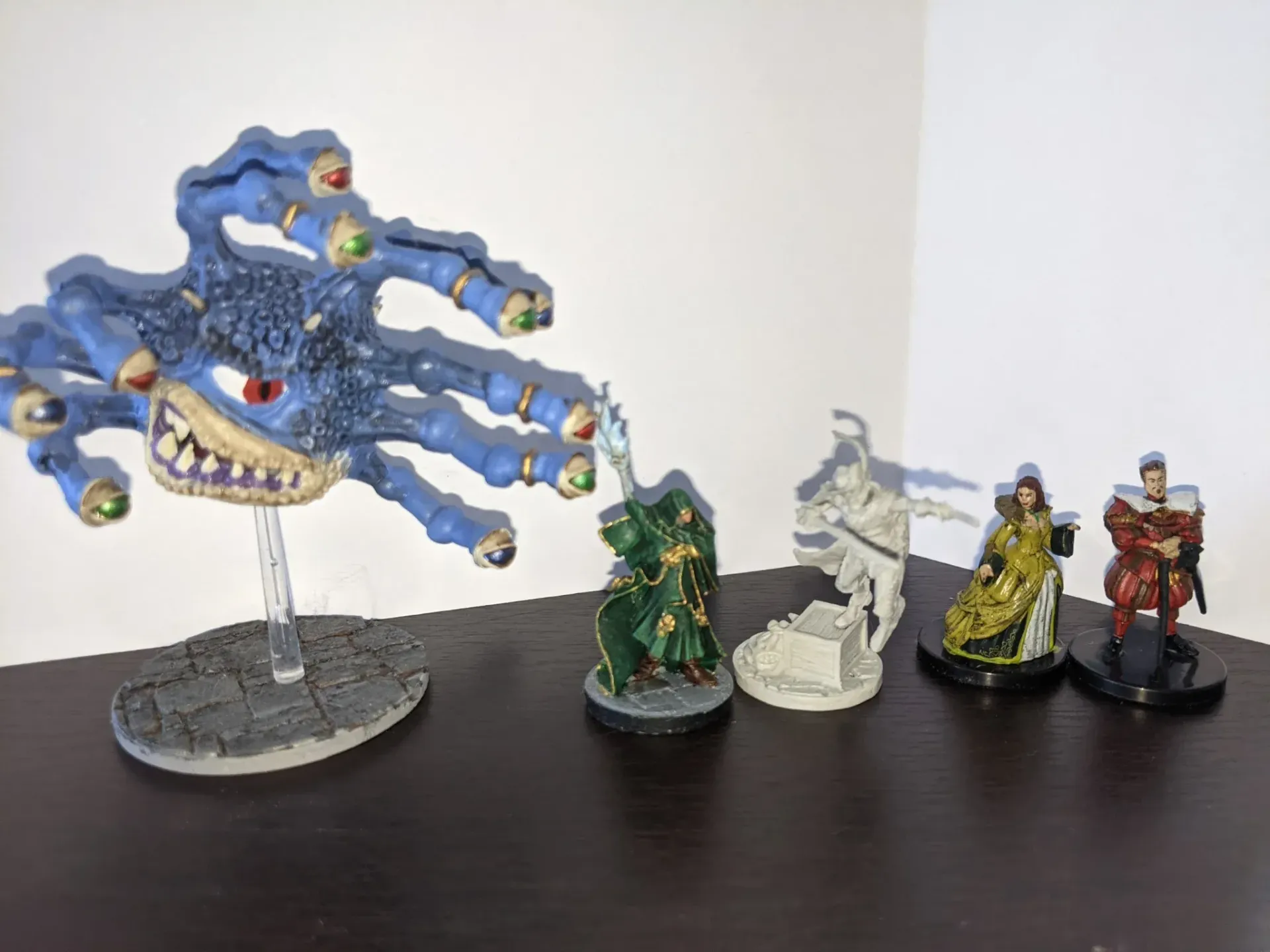 A blue Beholder miniature faces four smaller D&D figurines on a dark surface.