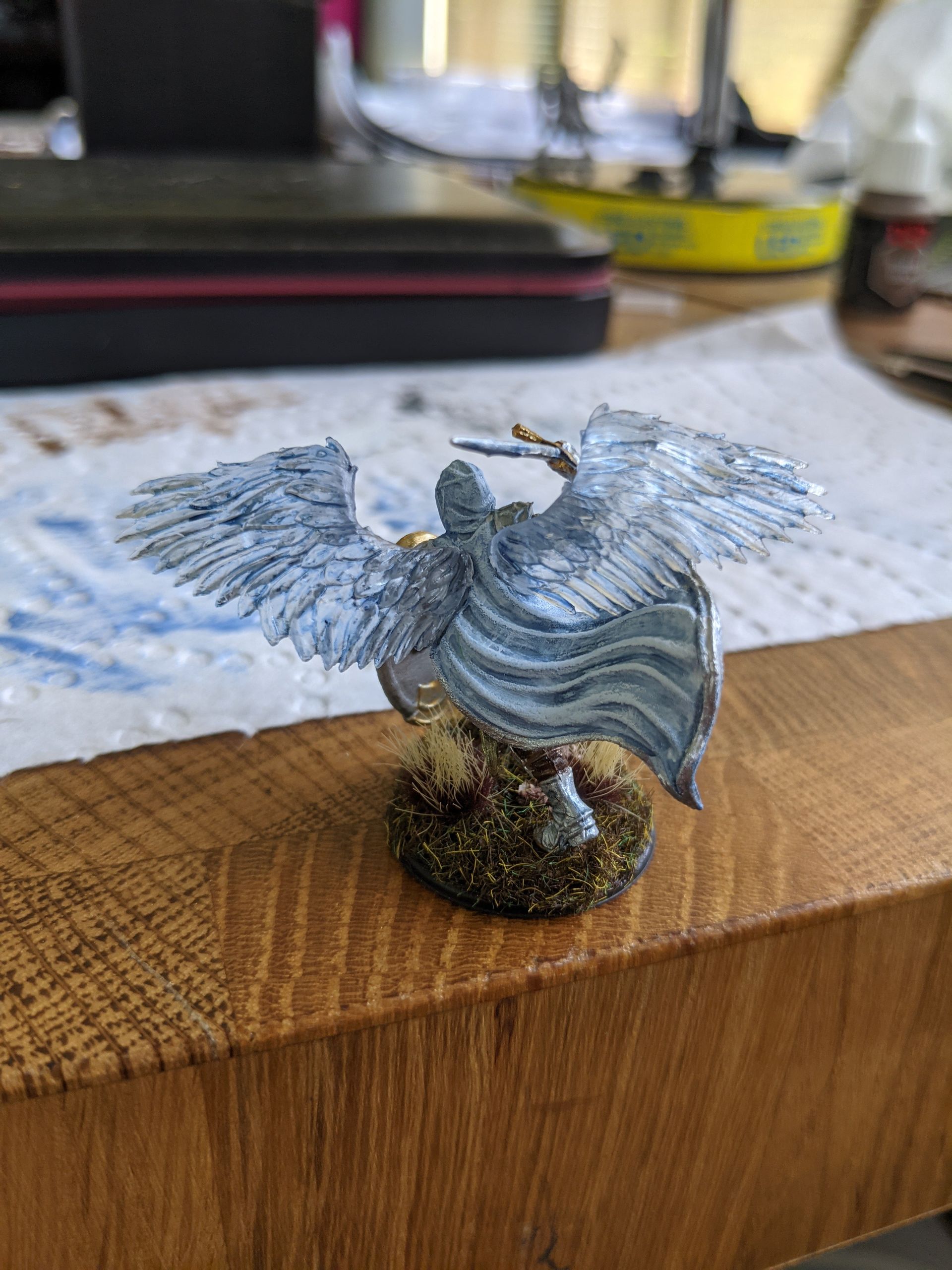 Miniature figure of a winged person painted with blue-grey tones, standing on a mossy, rocky base.