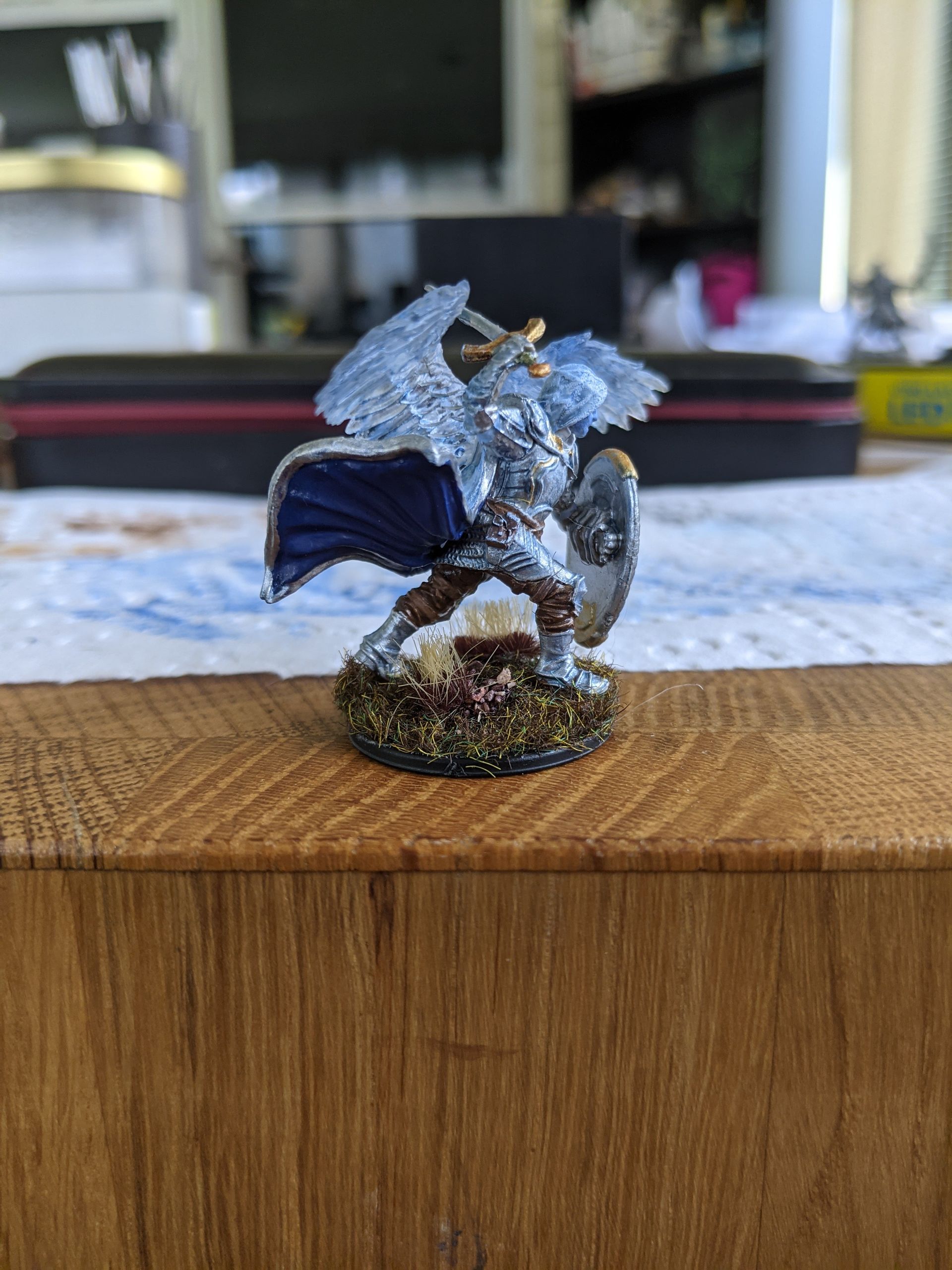 Miniature figure of an angel warrior with silver armor, blue cape, and wings, on a decorated base.