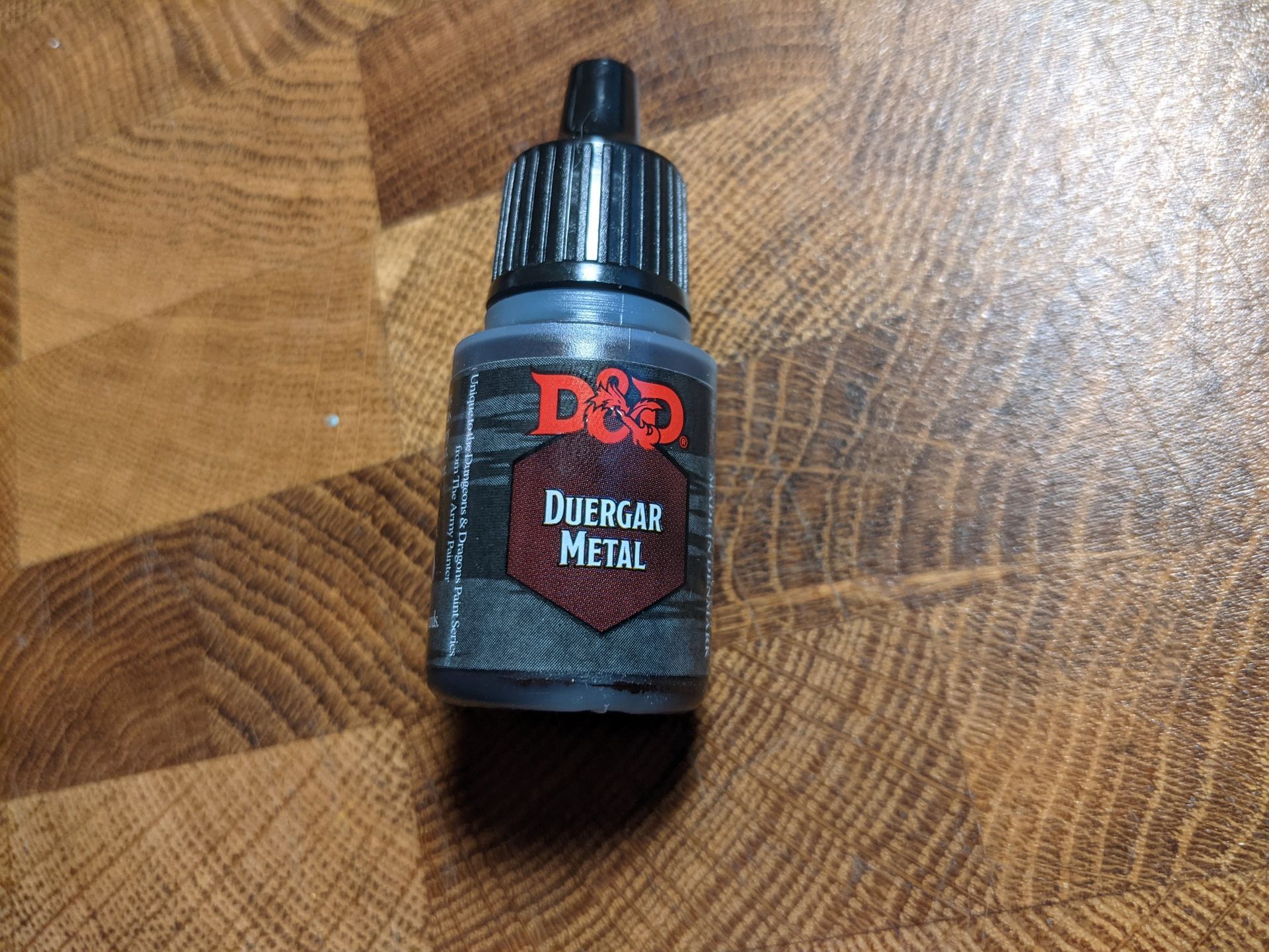 Bottle of D&D Dolagar Metal paint, label with red logo, set on a wood-grain surface.