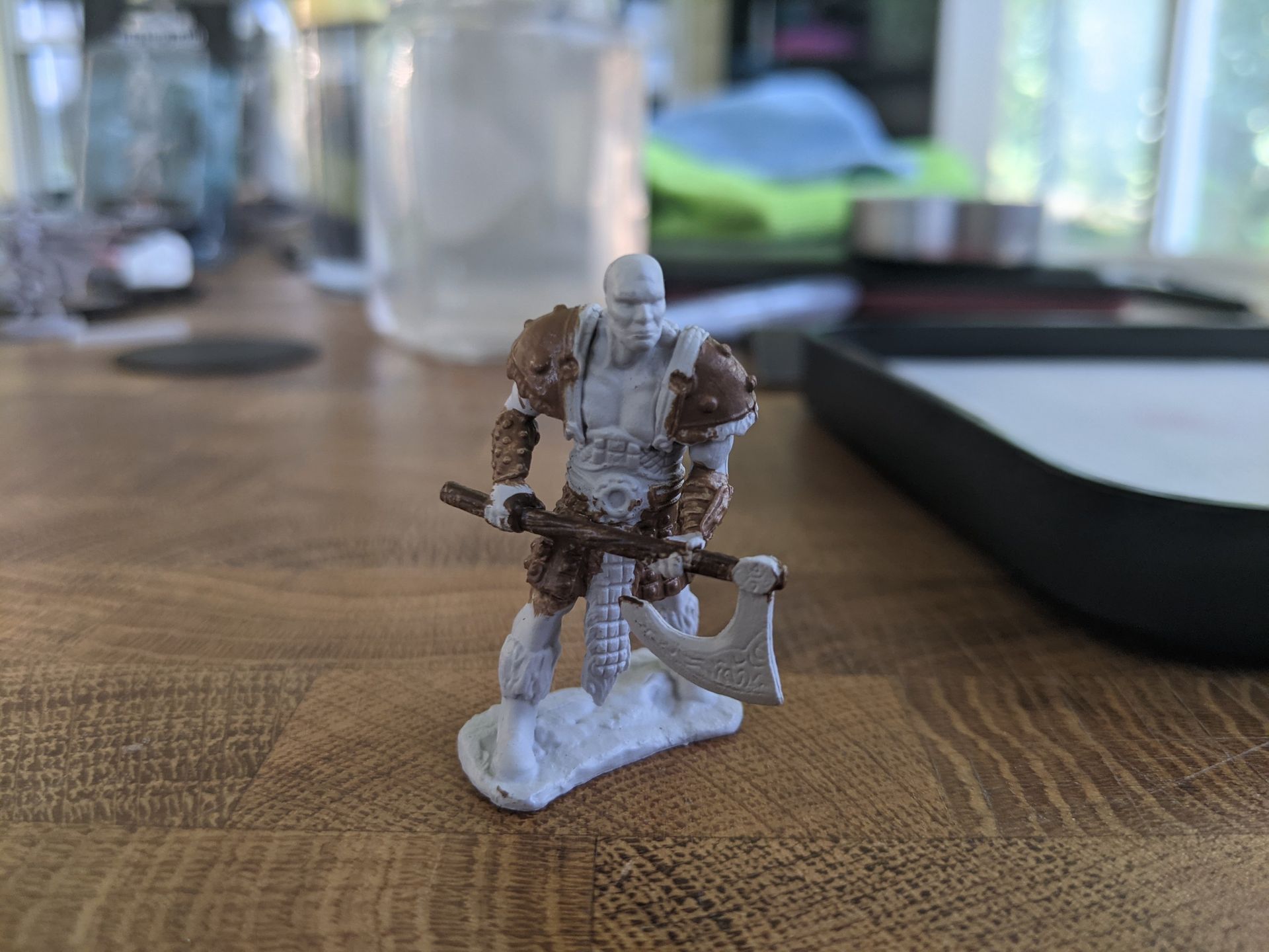 Miniature figure of a bald, skeletal warrior with brown fur, axe, and shoulder pads, on a wooden table.