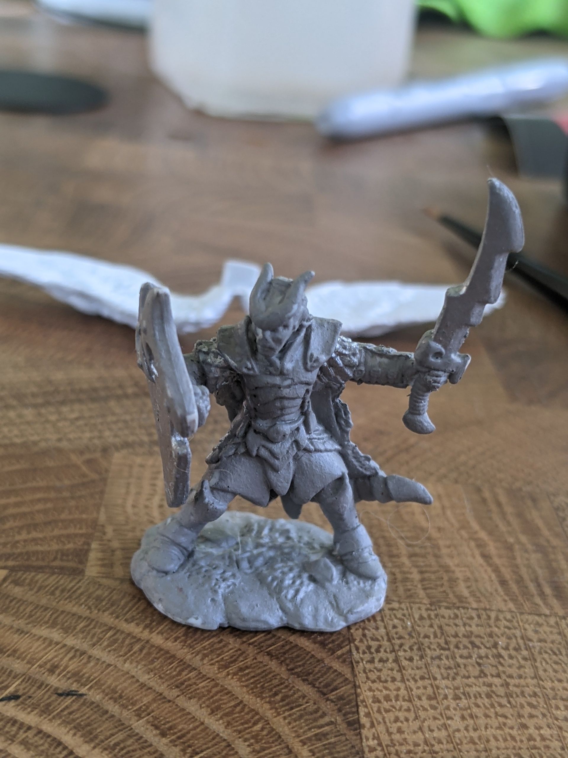 Miniature warrior figure, wielding curved blades, stands on a rocky base.