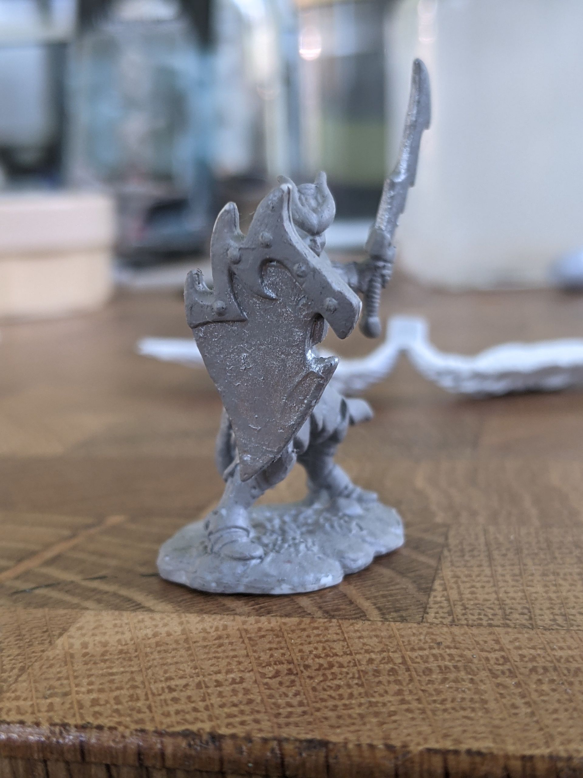 A small, grey fantasy warrior figure with sword and shield, standing on a textured base.