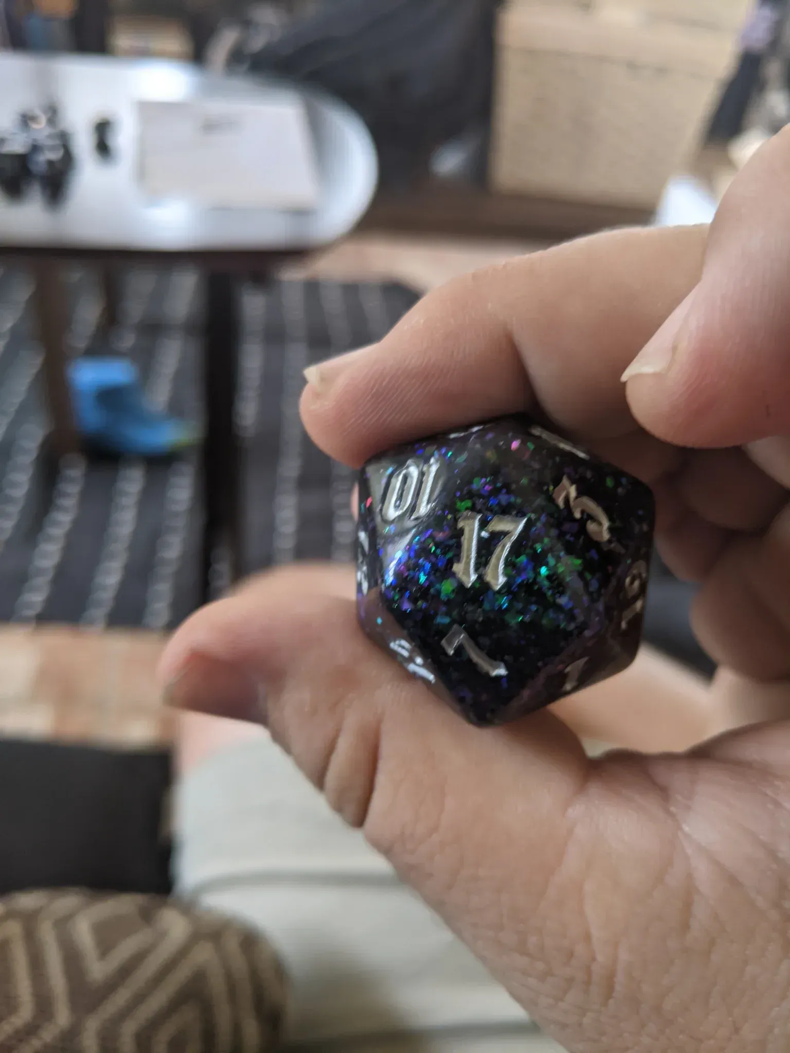 A hand holds a large, sparkly, multi-sided die. The numbers are white.