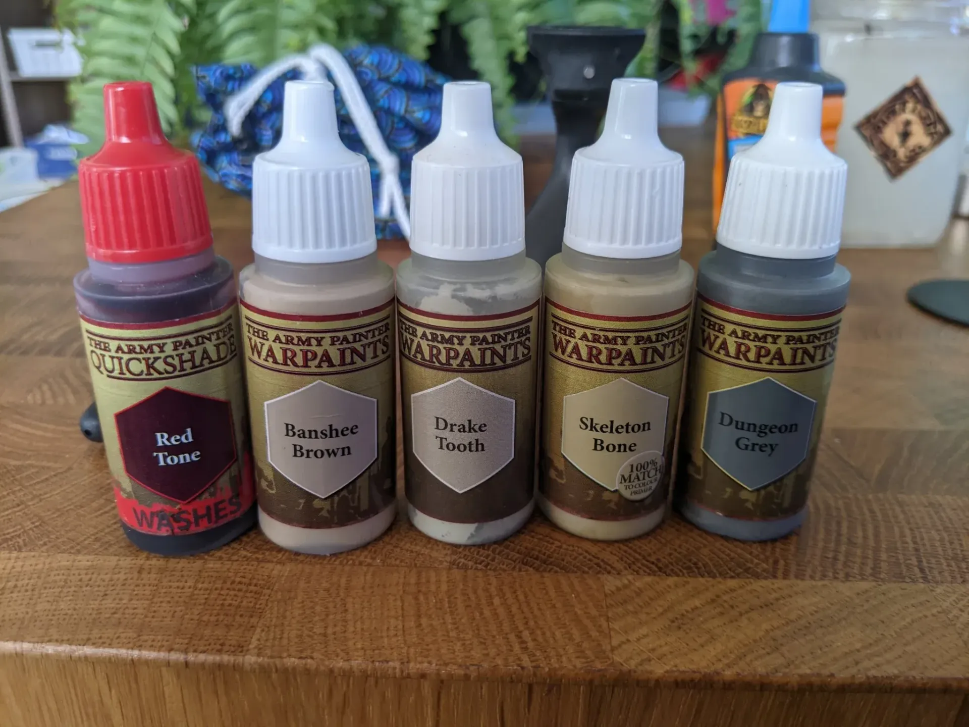Five Army Painter Warpaints in a row: red, beige, grey-brown, light beige, and grey.