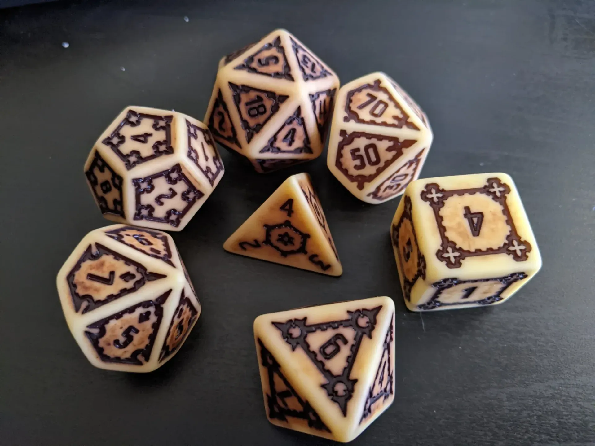 Set of ivory-colored dice with brown numerals and decorative borders on a dark surface.