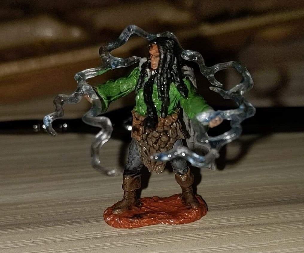 Miniature of a wizard, green robe, long dark hair, casting magic with blue ethereal swirls.