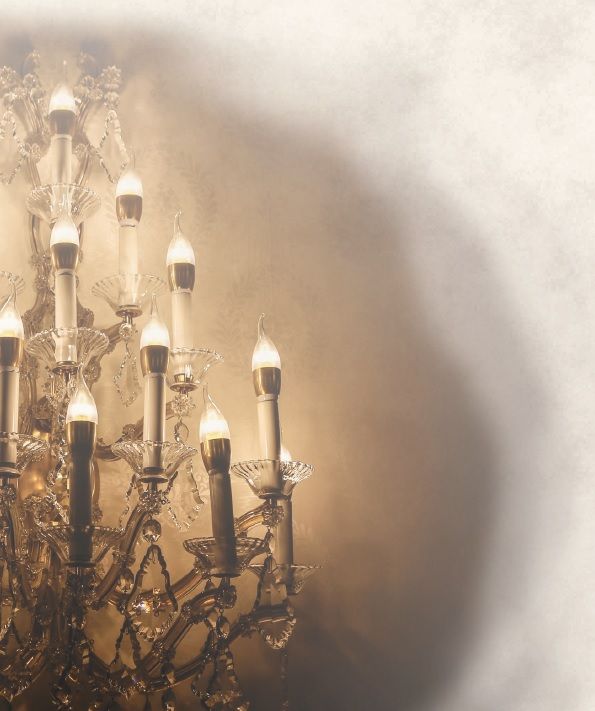 Ornate chandelier, illuminated with warm lights, casting shadows on a light-colored wall.