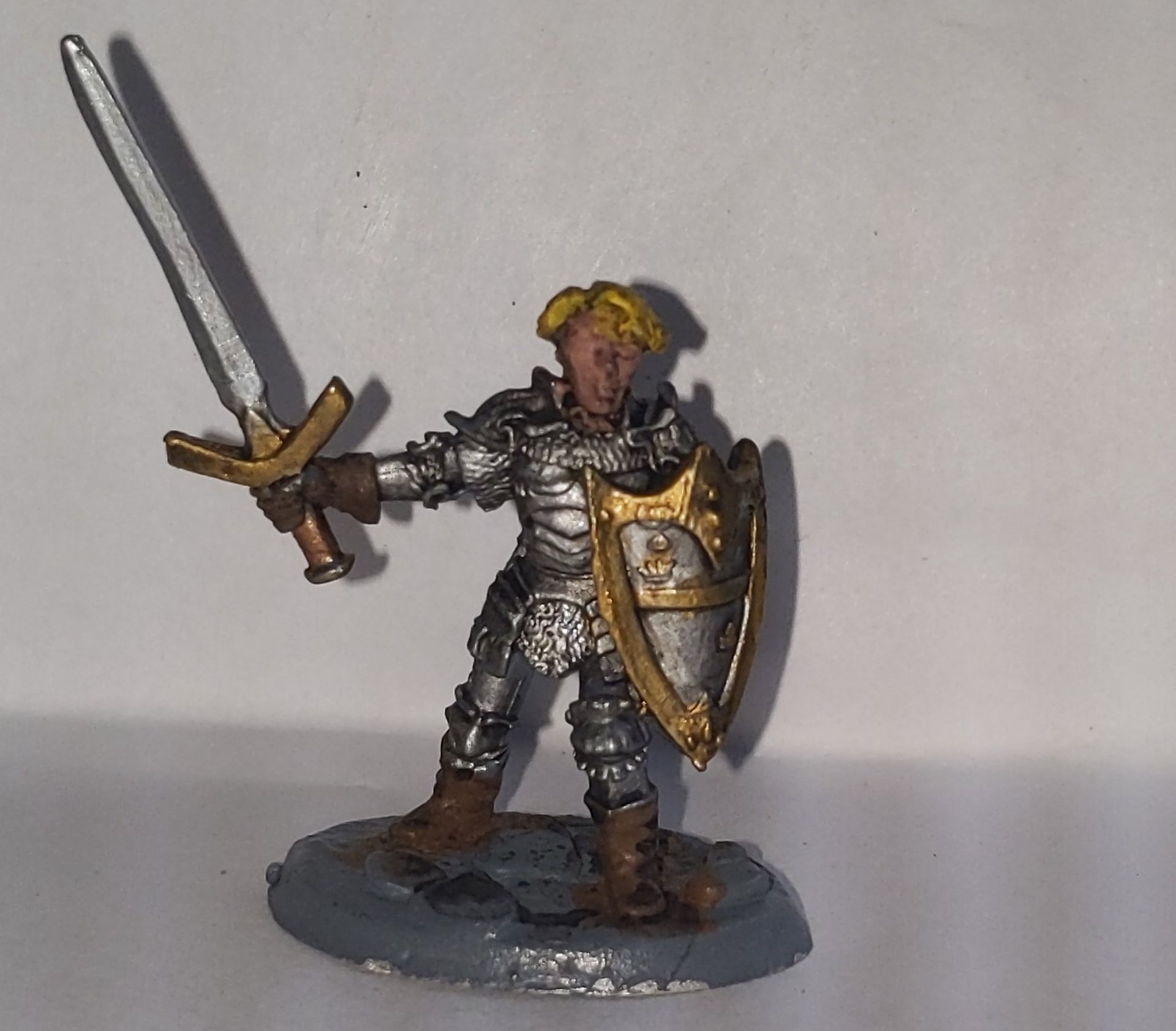 Miniature knight in silver armor, blonde hair, holding sword and shield.