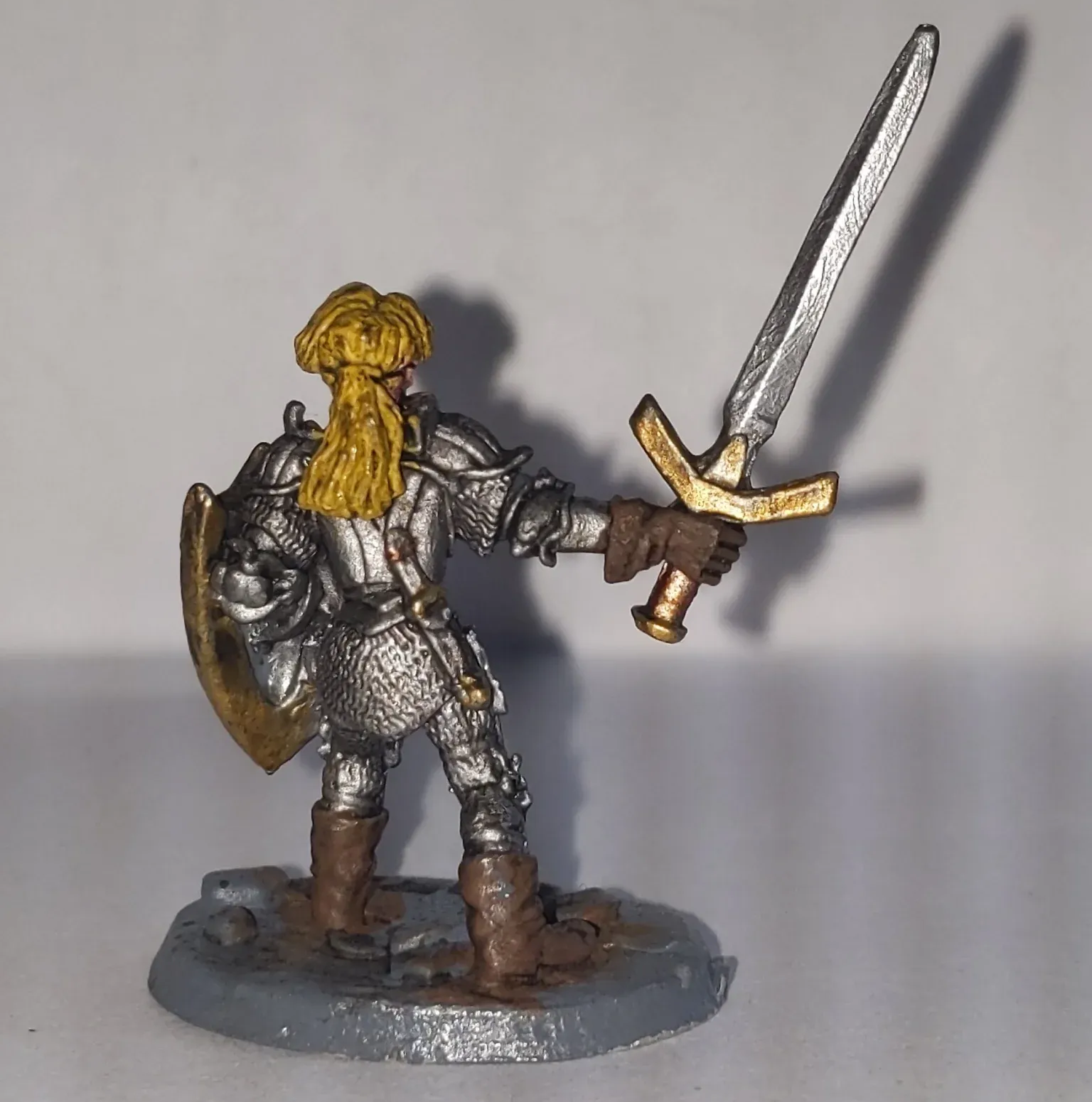 Miniature figure of a knight in silver armor holding a sword and shield, blonde hair, brown boots, gray base.